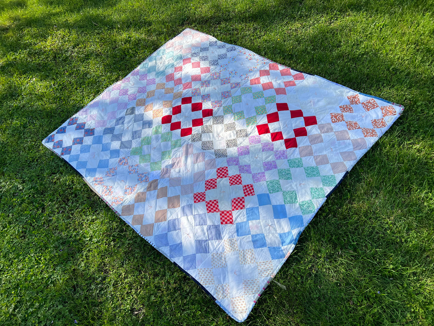 a beautiful vintage quilt, which has been mended and re-bound, lays on a plush green lawn. Splotches of sunshine dance across the quilt top