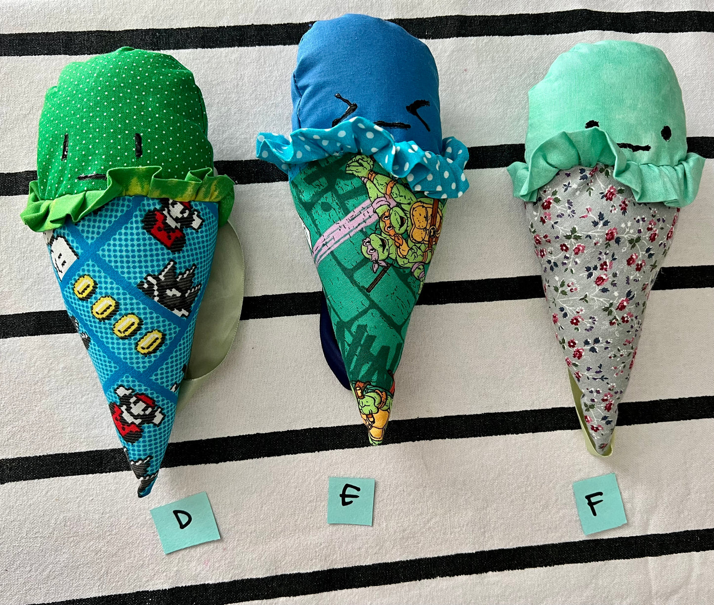 Ice cream cone plushies with handpainted faces, lined up with the letters D E F below them