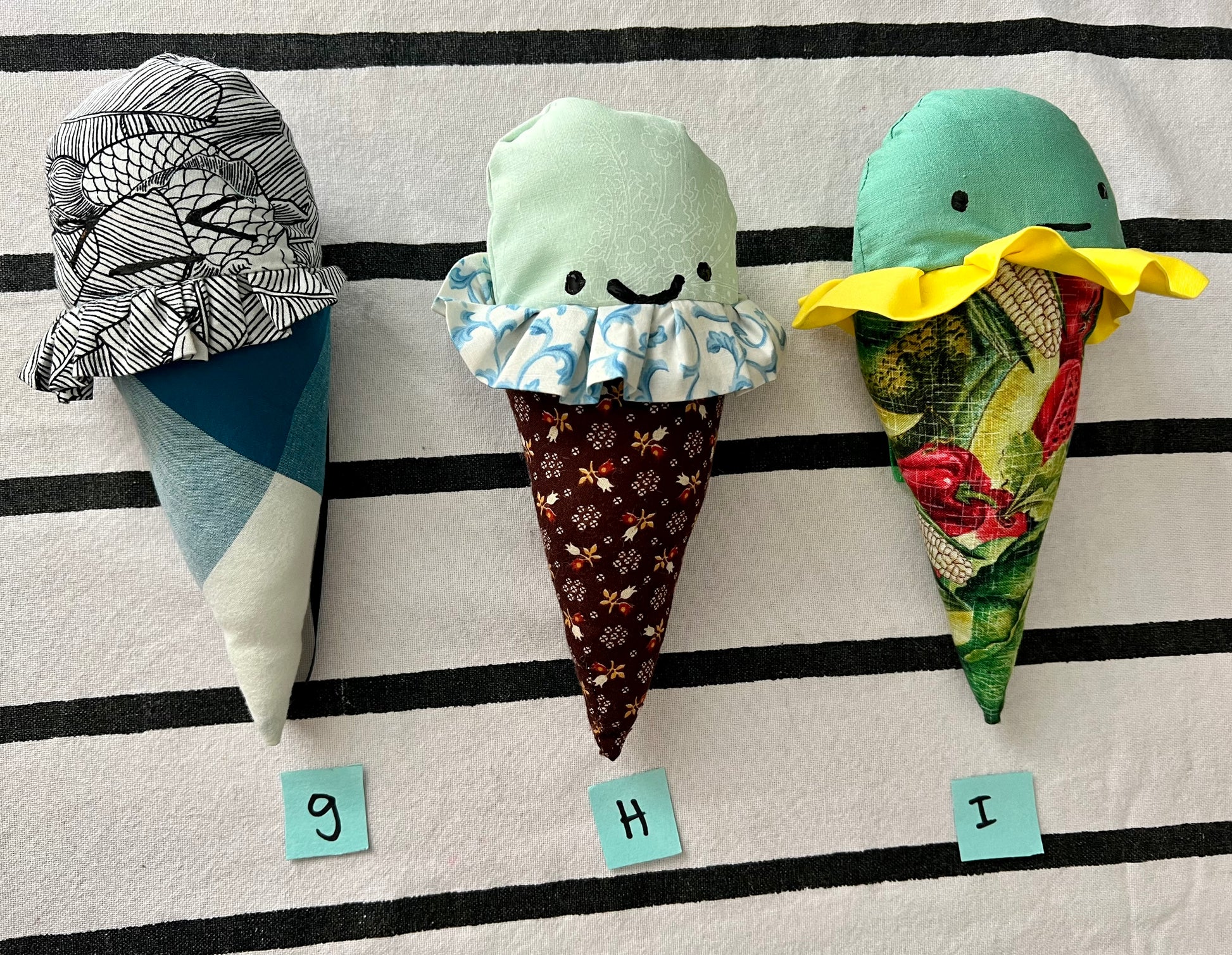 Ice cream cone plushies with handpainted faces, lined up with the letters G H I below them
