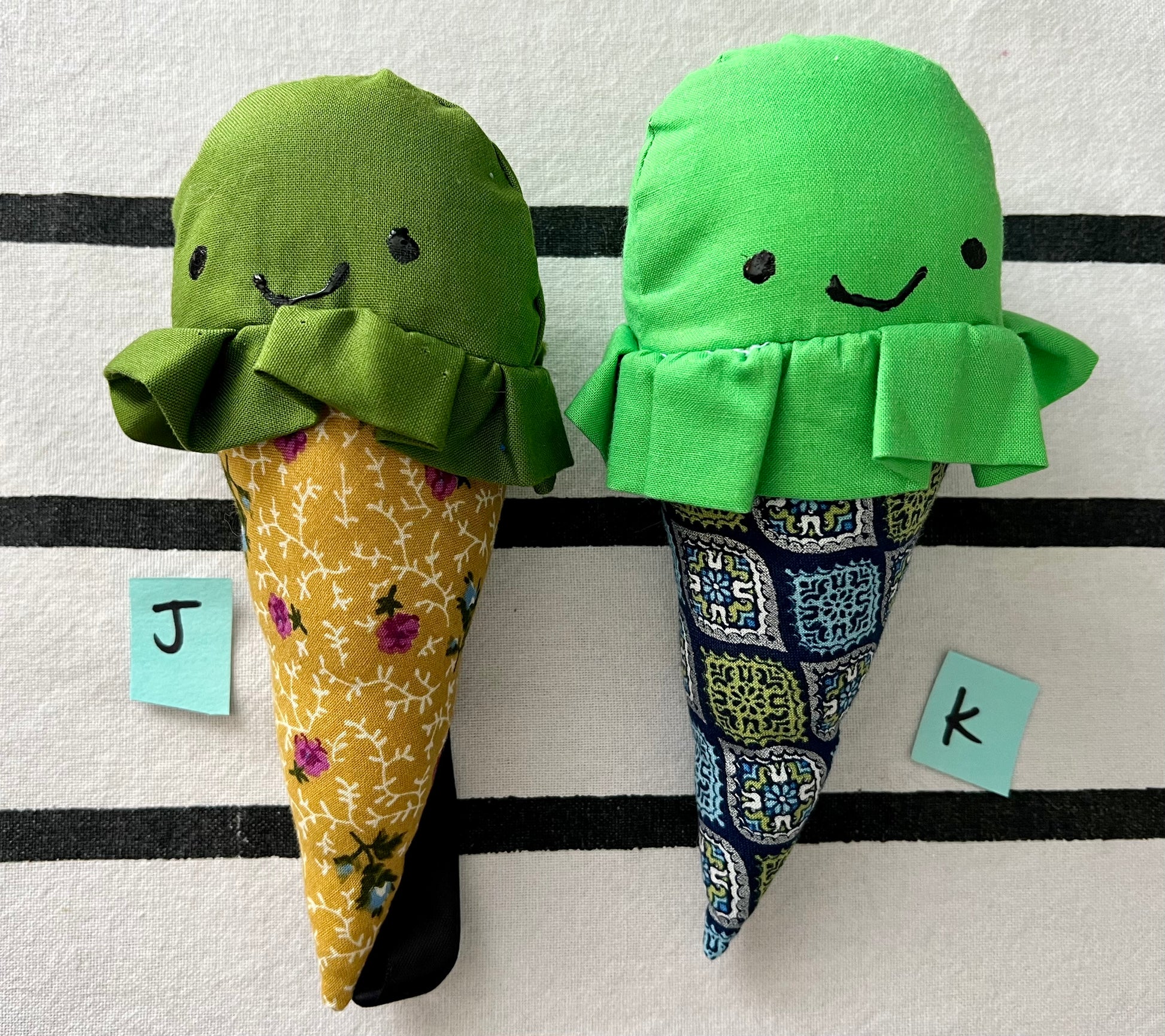 Ice cream cone plushies with handpainted faces, lined up with the letters J K below them