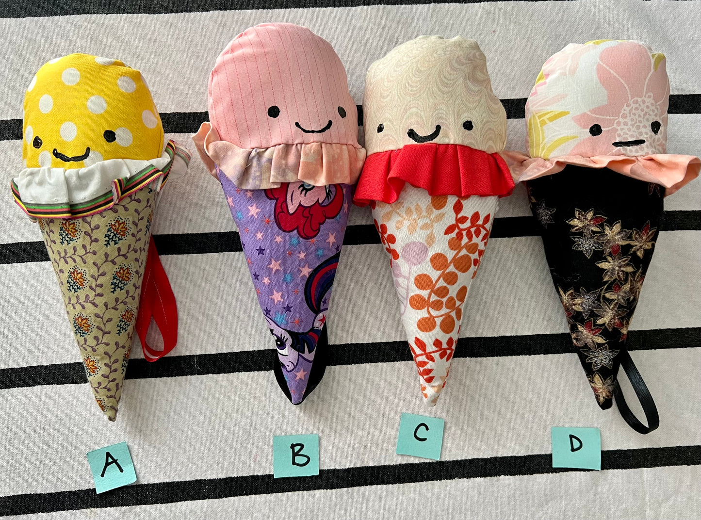 Ice cream cone plushies with handpainted faces, lined up with the letters A B C D below them