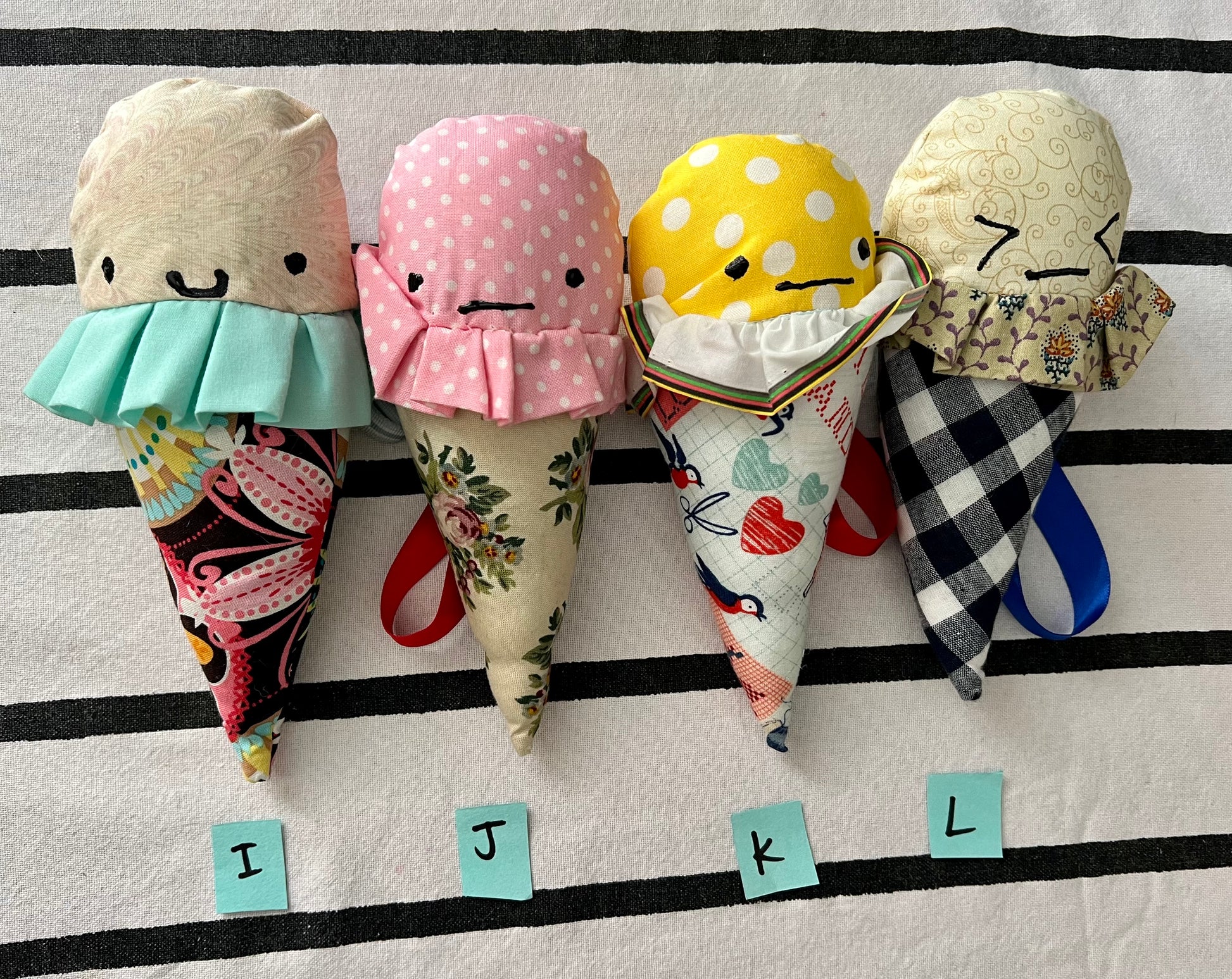 Ice cream cone plushies with handpainted faces, lined up with the letters I J K L below them