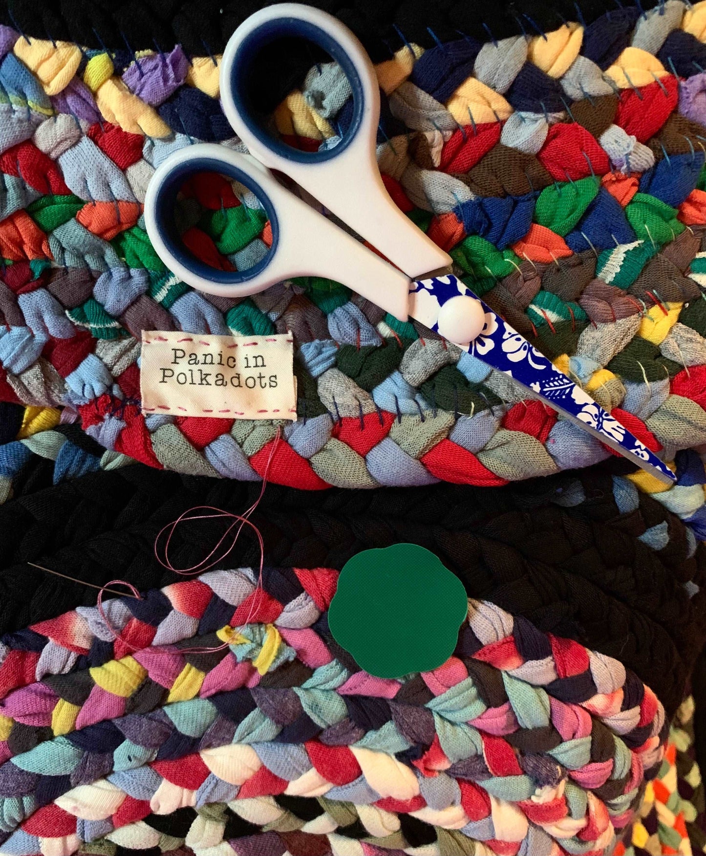 closeup view of work in progress, as label gets sewn on. scissors, needle and thread, and needle puller are on top of rug