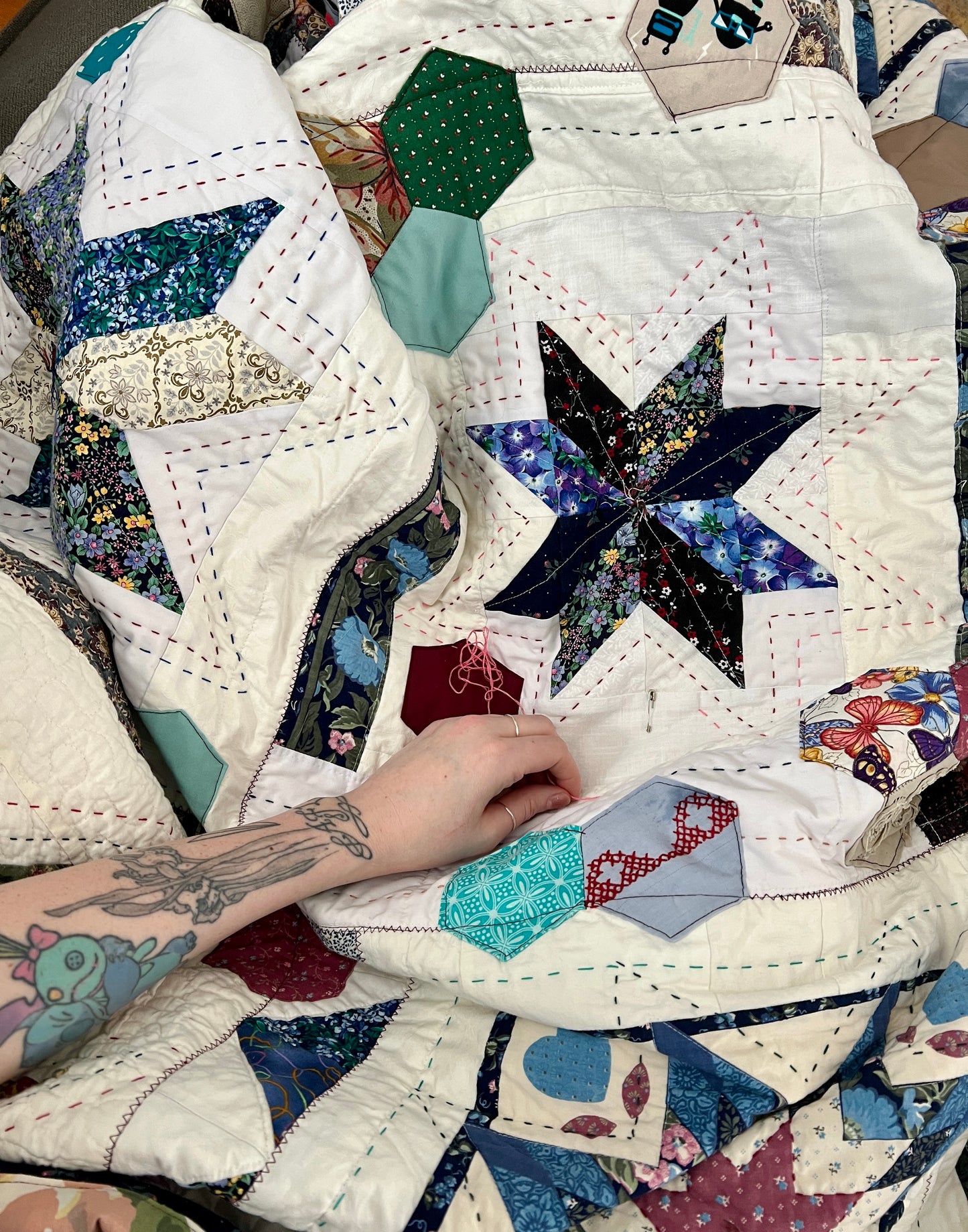 eight point stars, and scrappy hexagons quilt, sas a work in progress, a tattooed arm across the top, with needles and thread in hand