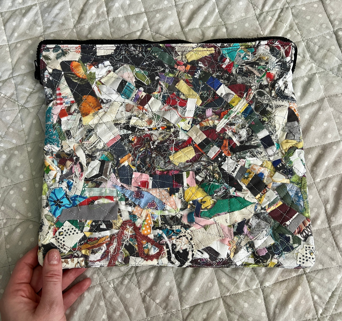a padded zipper case which will fit an ipad, with various fabric and thread scraps sewn beneath a mesh layer