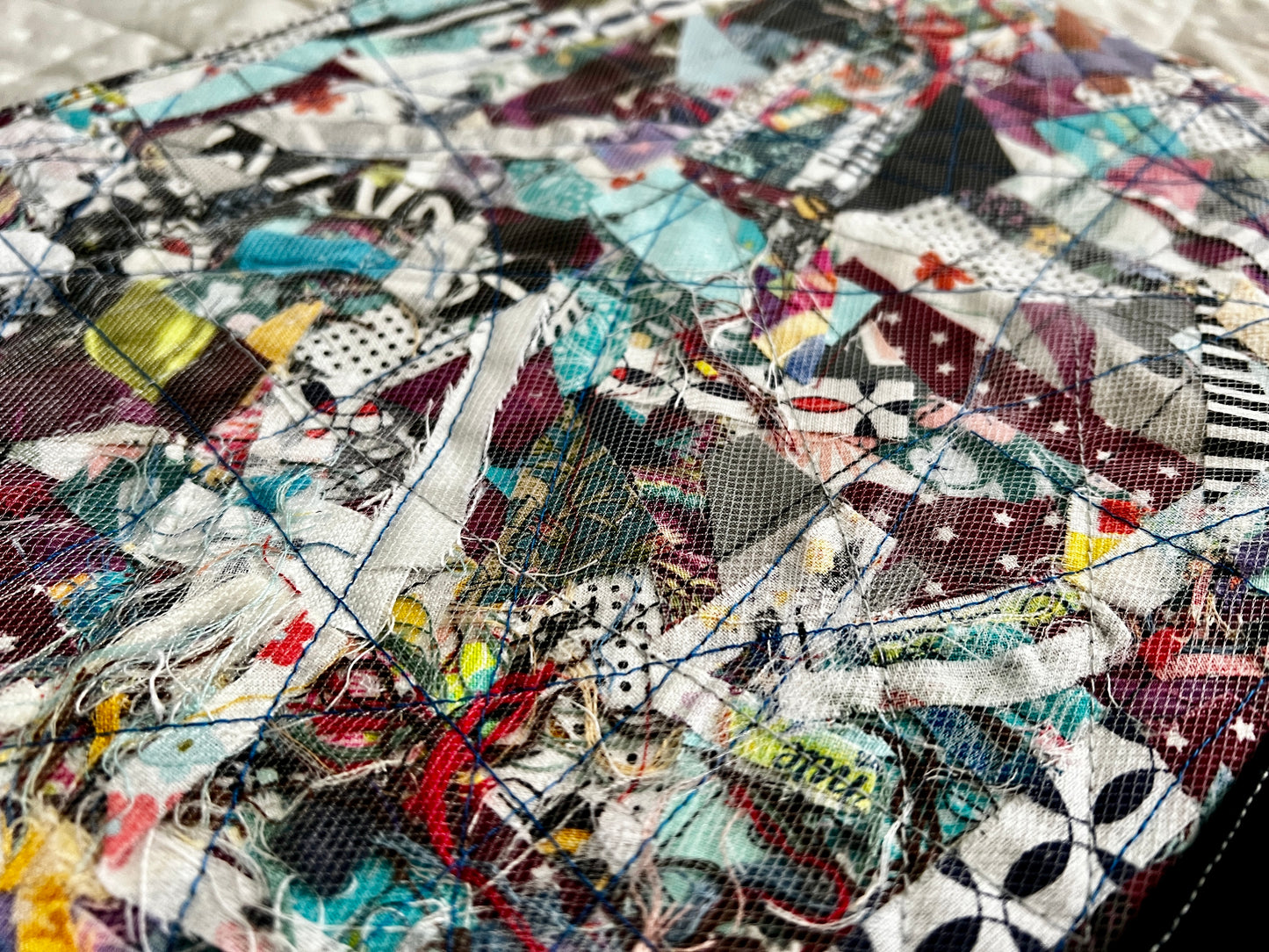 ipad scrappy case closeup, fabric scraps and thread scraps are shown beneath a mesh, with several enforcing stitches across in every direction
