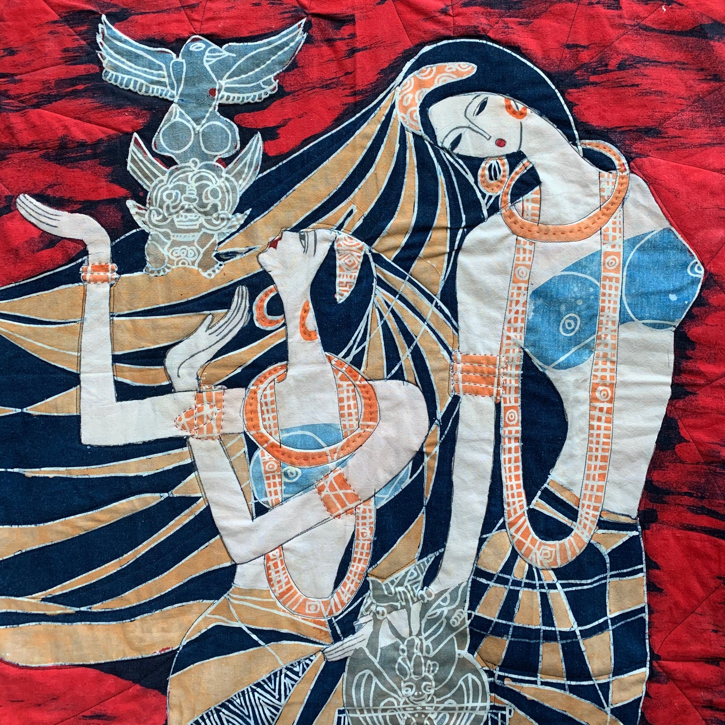 Closeup of deities and totems, with handquilted details on necklaces, jewelry, and quilted lines throughout the red background