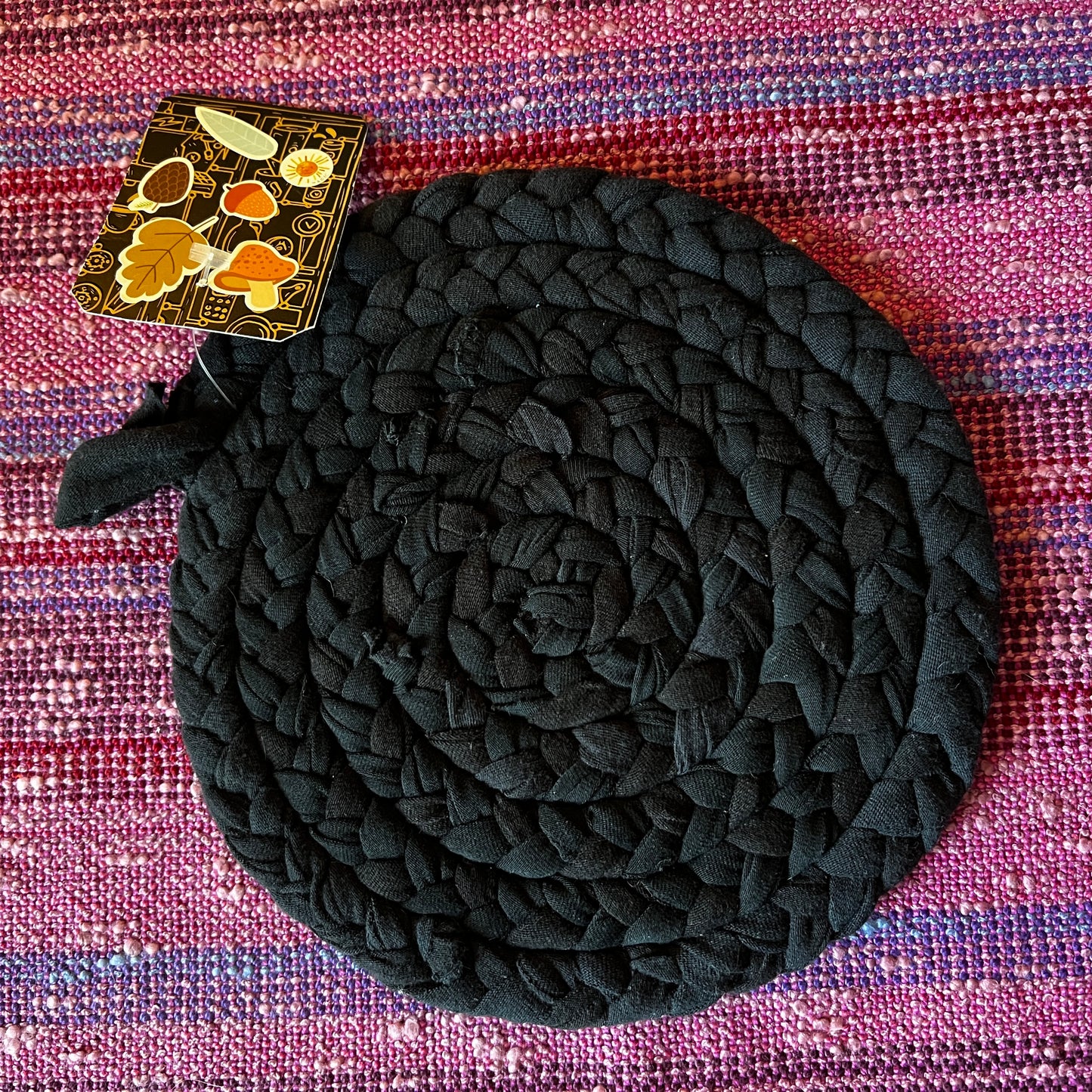single hand braided and hand sewn potholder/trivet flat lay against a bright pink background