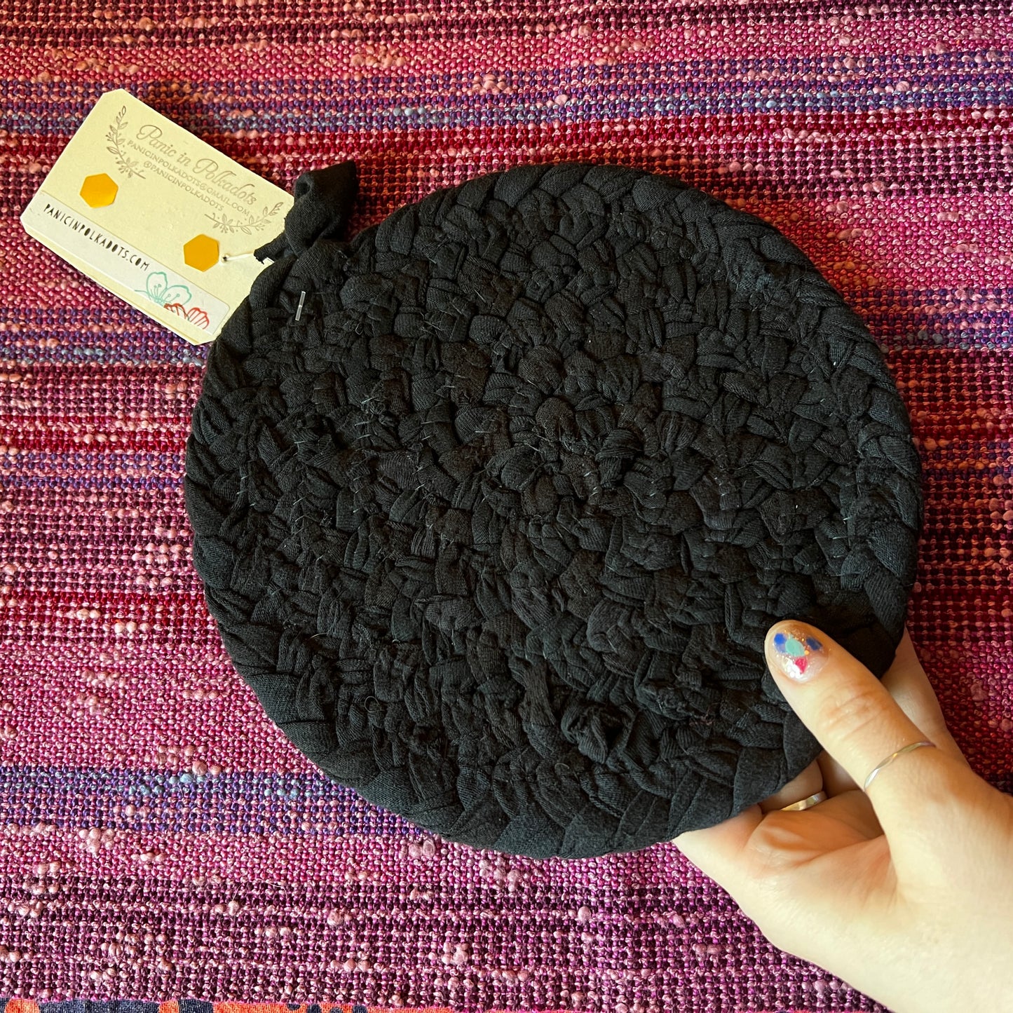 single hand braided and hand sewn potholder/trivet held up against a bright pink background