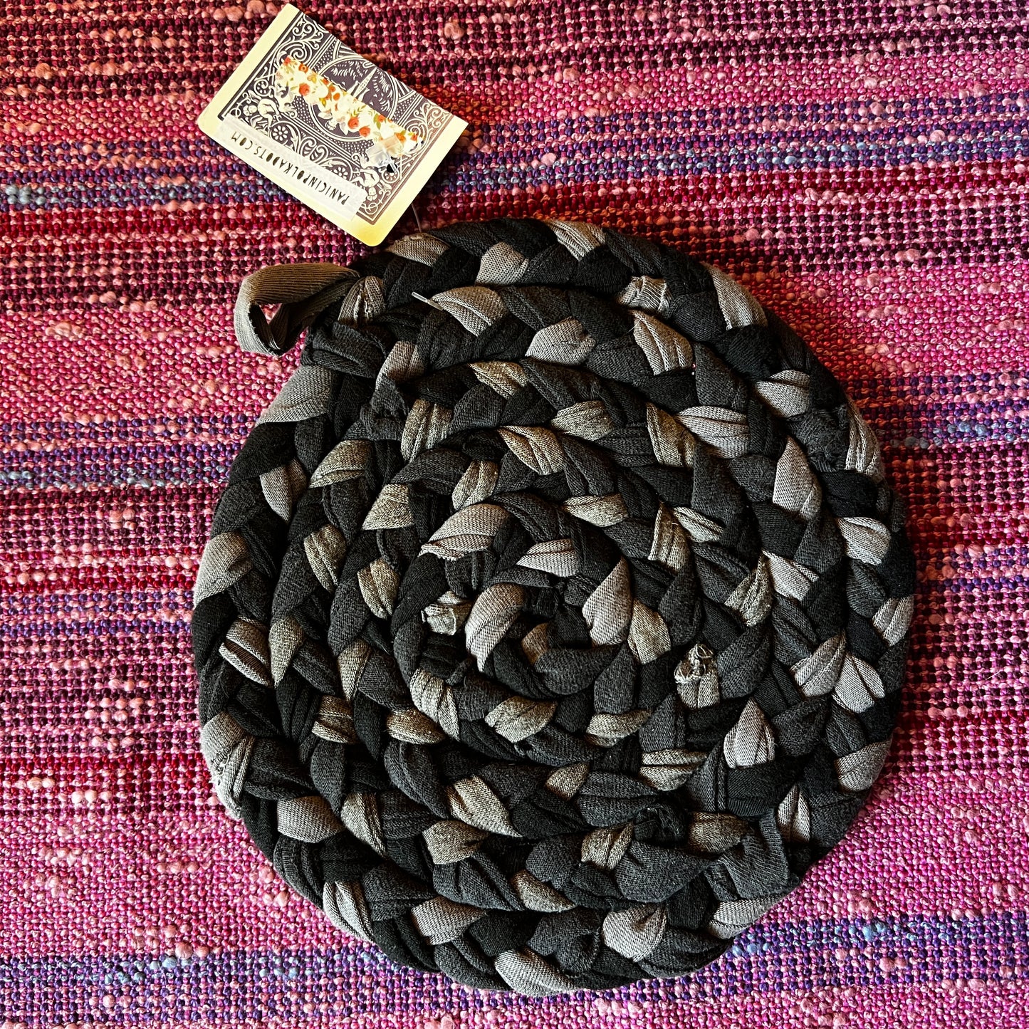 single hand braided and hand sewn potholder/trivet lay flat against a bright pink background