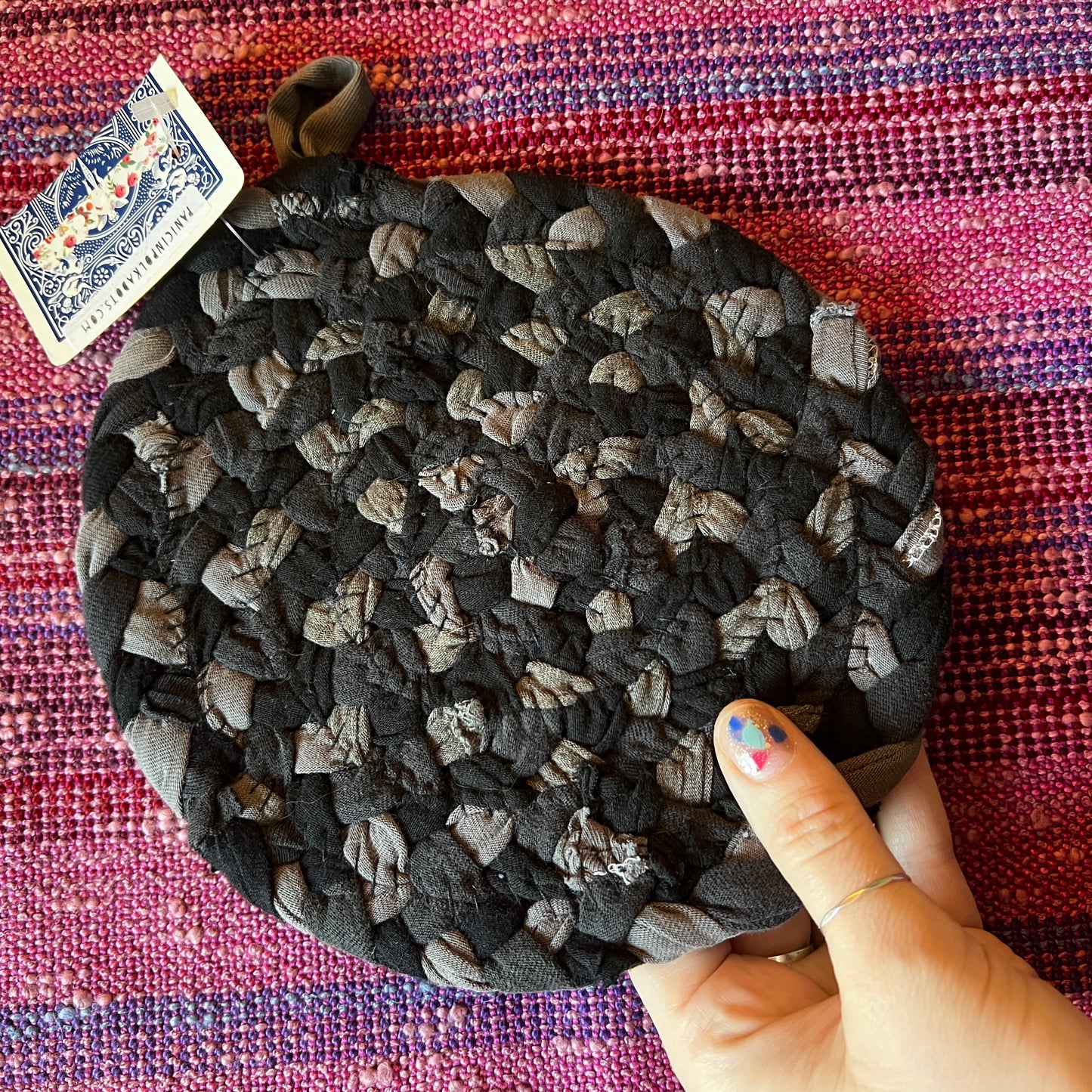 single hand braided and hand sewn potholder/trivet held up against a bright pink background