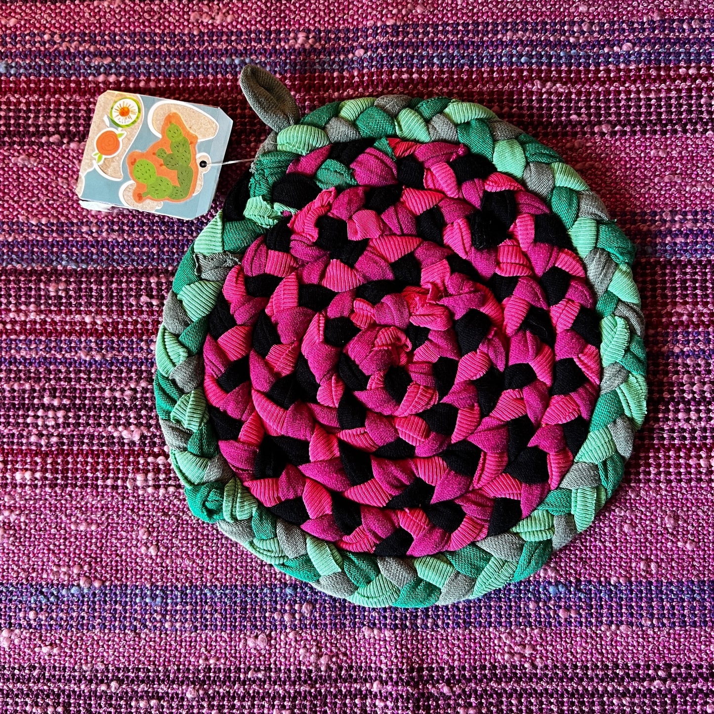 single hand braided and hand sewn potholder/trivet lay flat against a bright pink background