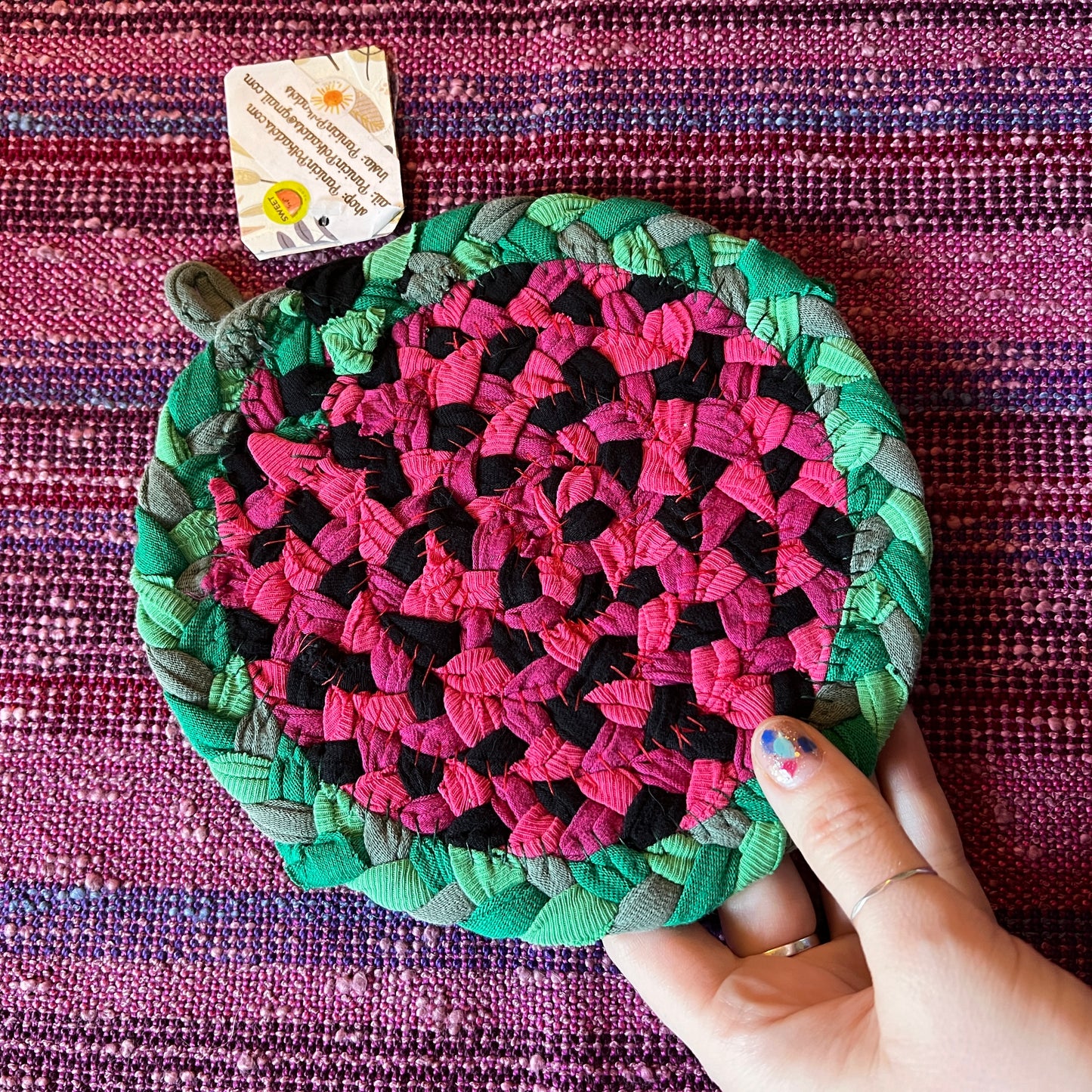 single hand braided and hand sewn potholder/trivet held up against a bright pink background