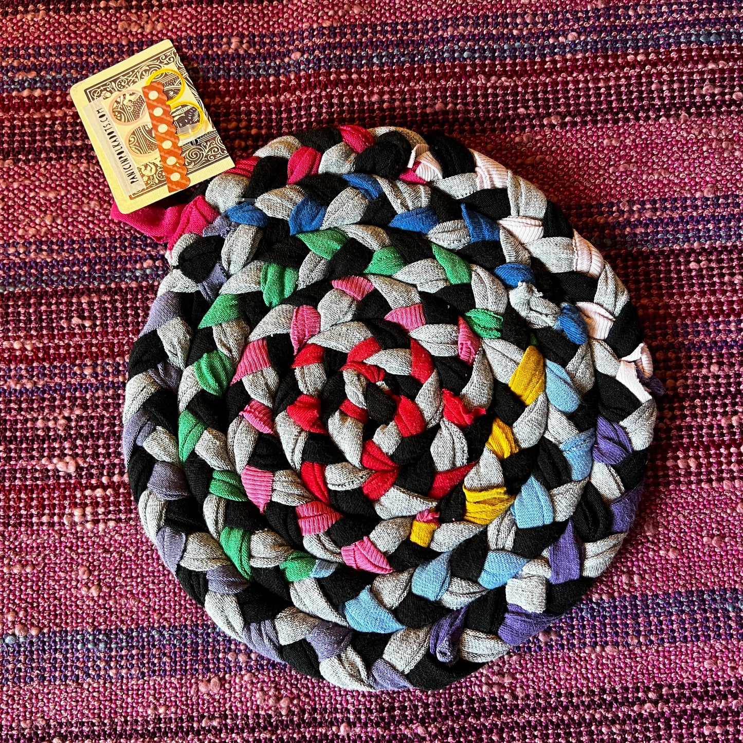 single hand braided and hand sewn potholder/trivet lay flat against a bright pink background