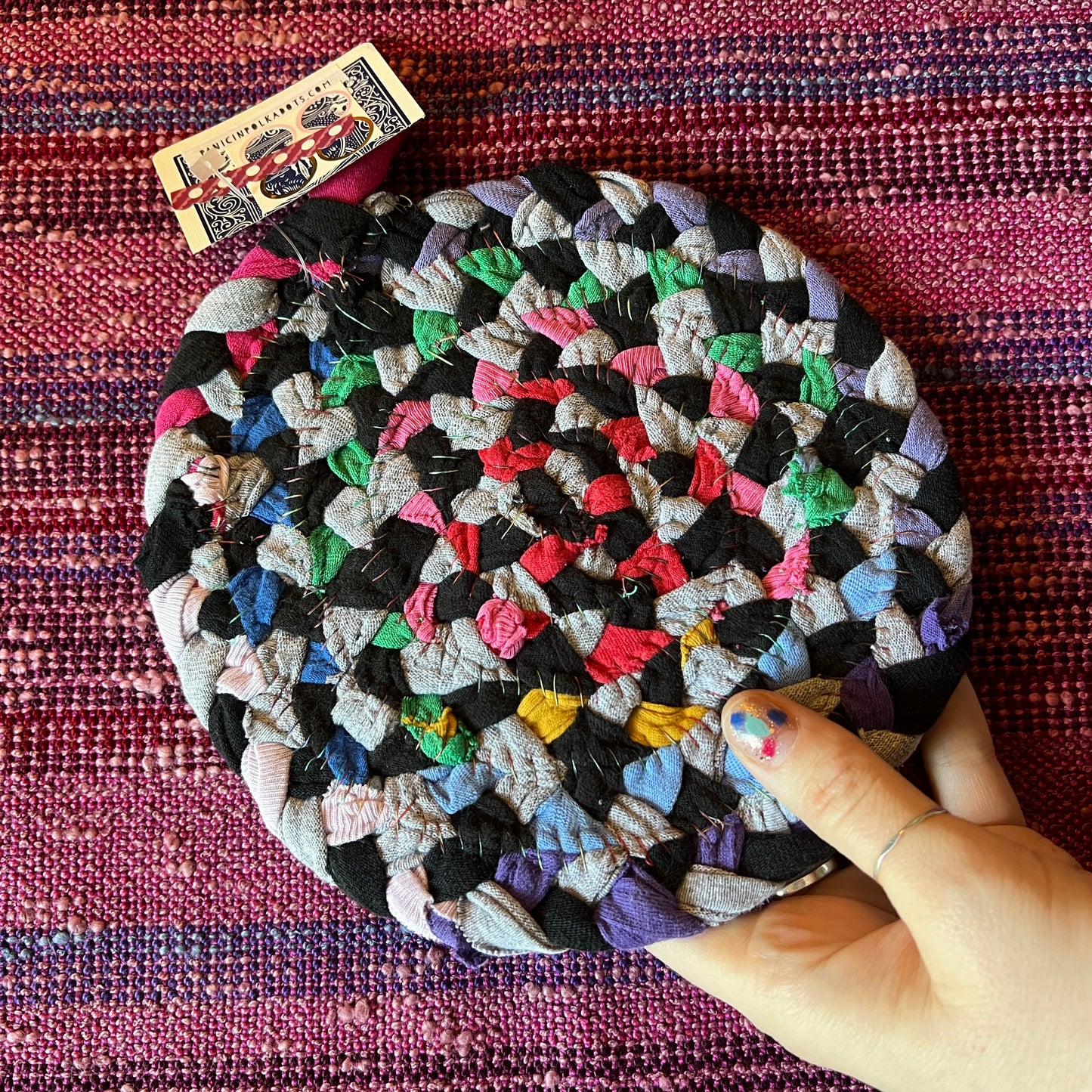 single hand braided and hand sewn potholder/trivet held up against a bright pink background