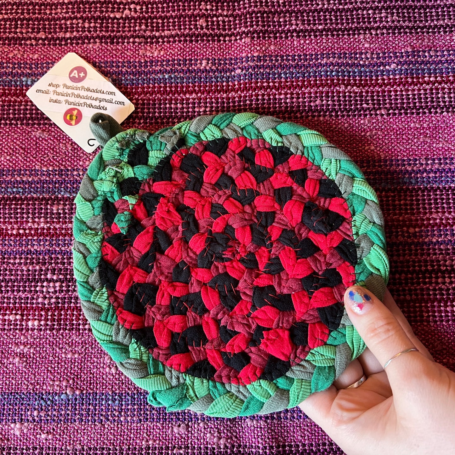 single hand braided and hand sewn potholder/trivet held up against a bright pink background,red watermelon