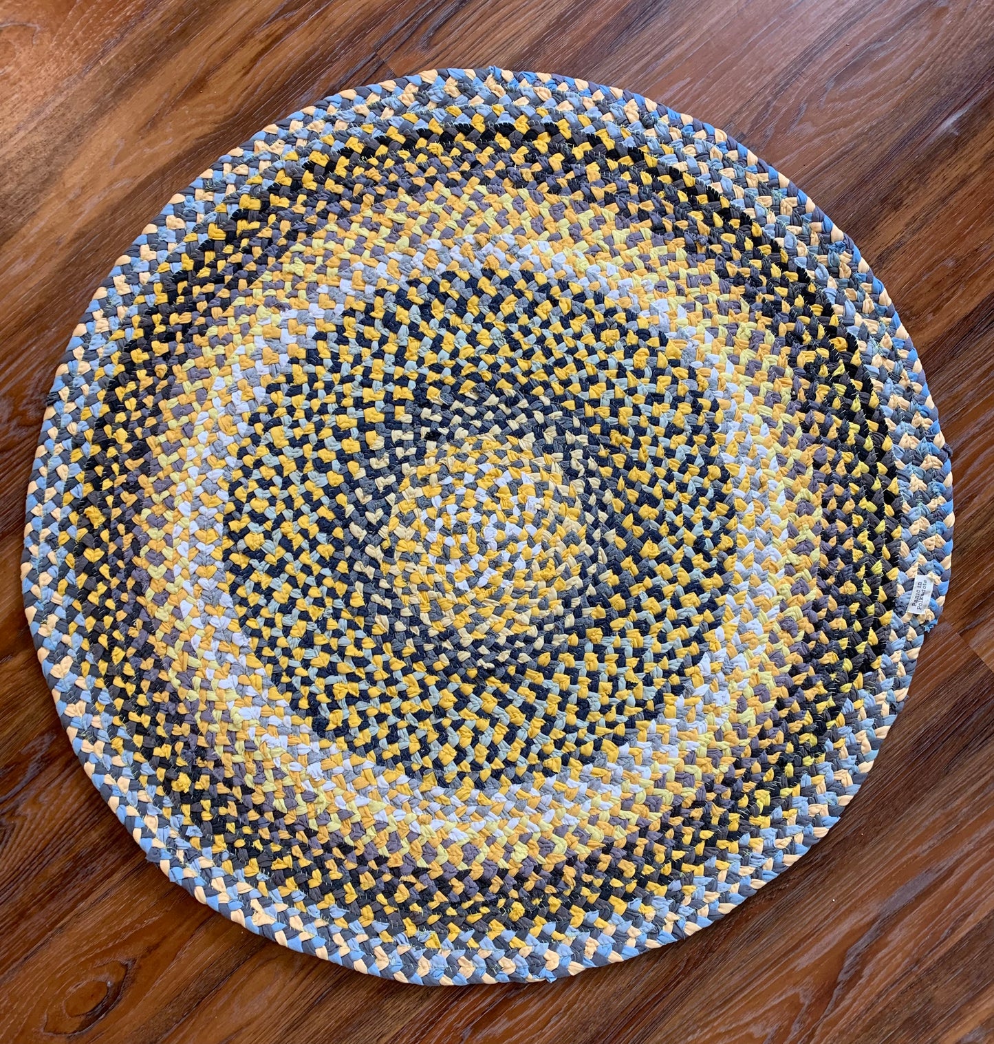 aerial view of t-shirt rug. Strands of yellow, grey, black, and white have been handbraided and handsewn into this design