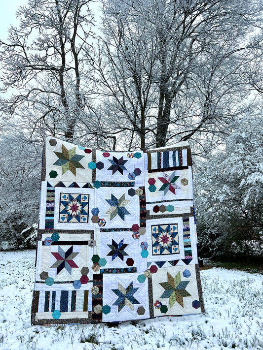 A quilt with eight point stars and quilted hexies, in a snowy scene