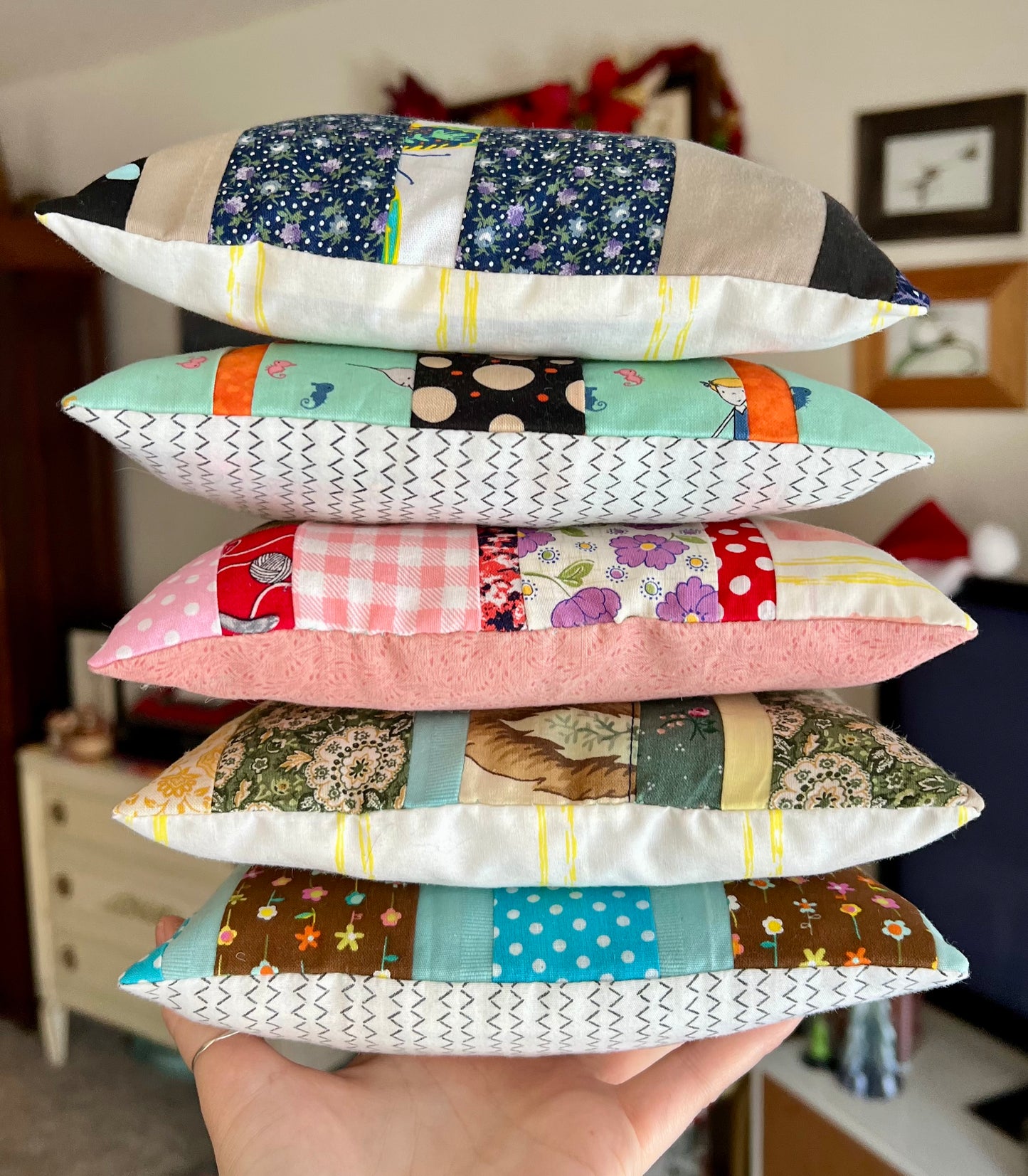 Stack of colorful patchwork pillows held in a hand with a blurred indoor background