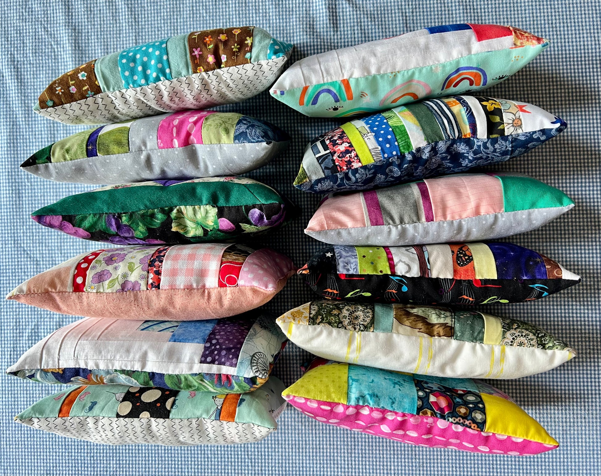 Twelve small rectangular patchwork doll pillows arranged in two columns on a blue-and-white checkered fabric background.