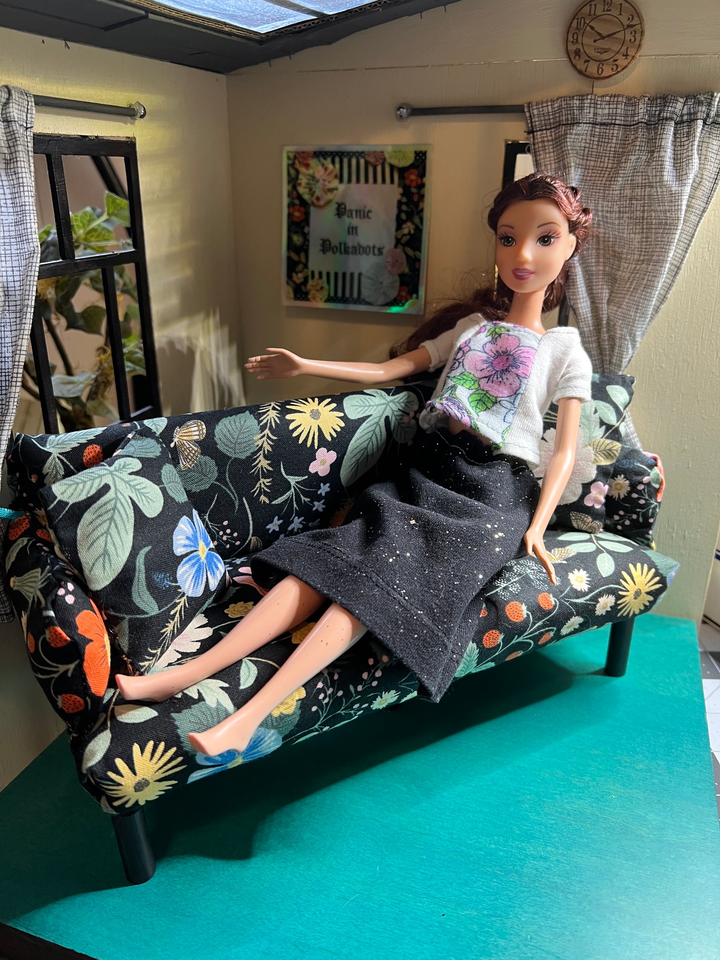 a Barbie doll sits across a miniature couch, with colorful flowers, in a 1:6 scale roombox