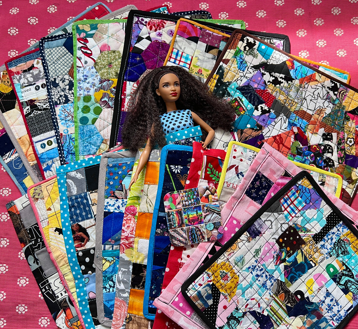Barbie doll surrounded by colorful quilted bags on a pink floral background