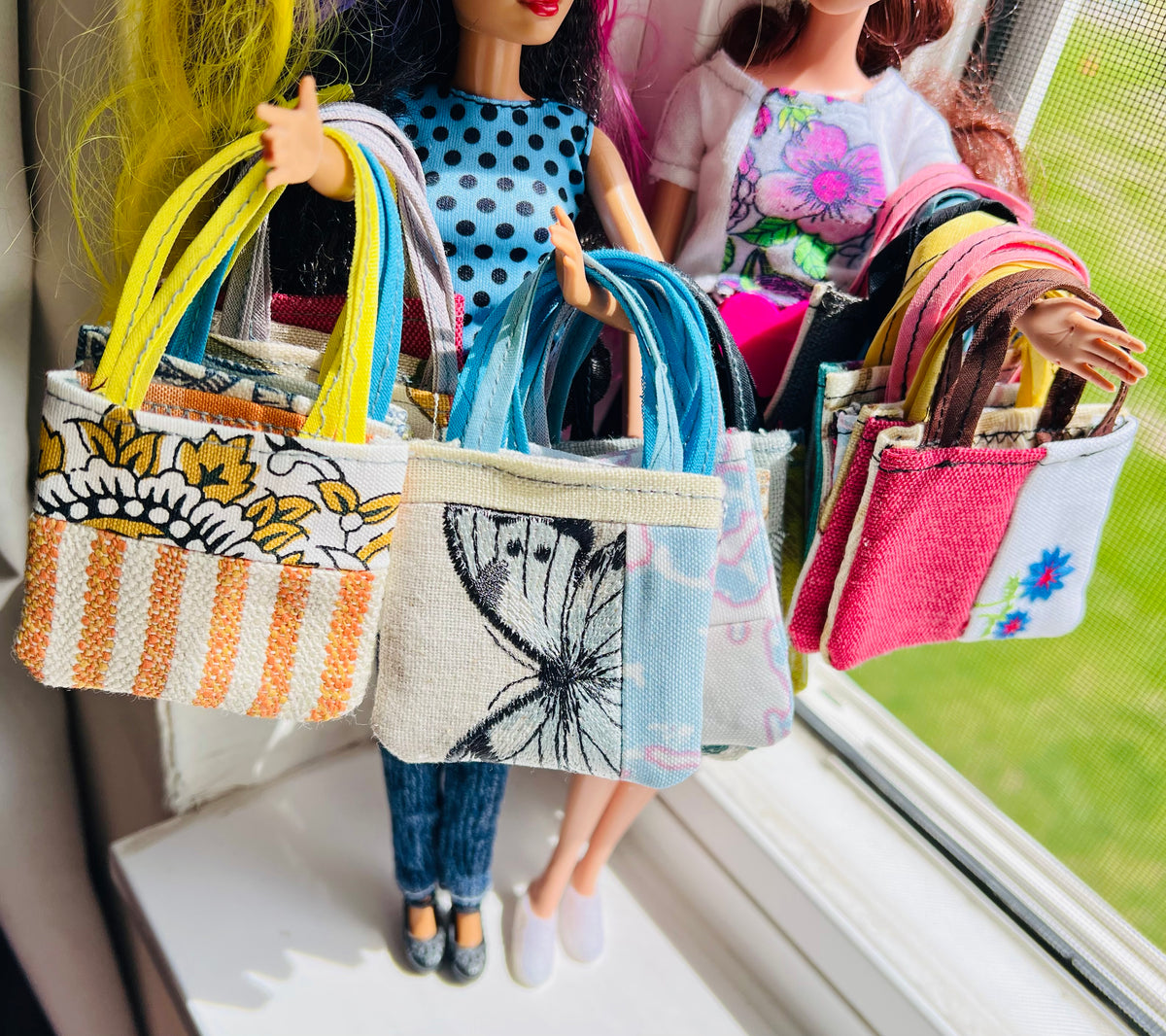 Barbie dolls holding colorful handbags by a window