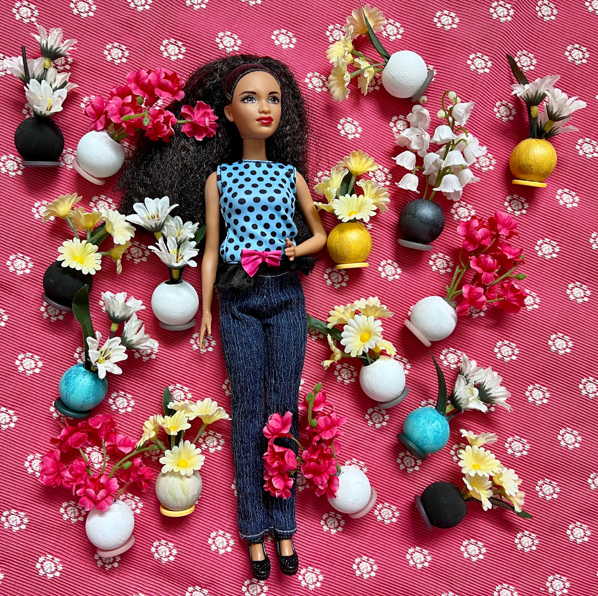 Barbie doll with a floral and vase arrangement on a pink background