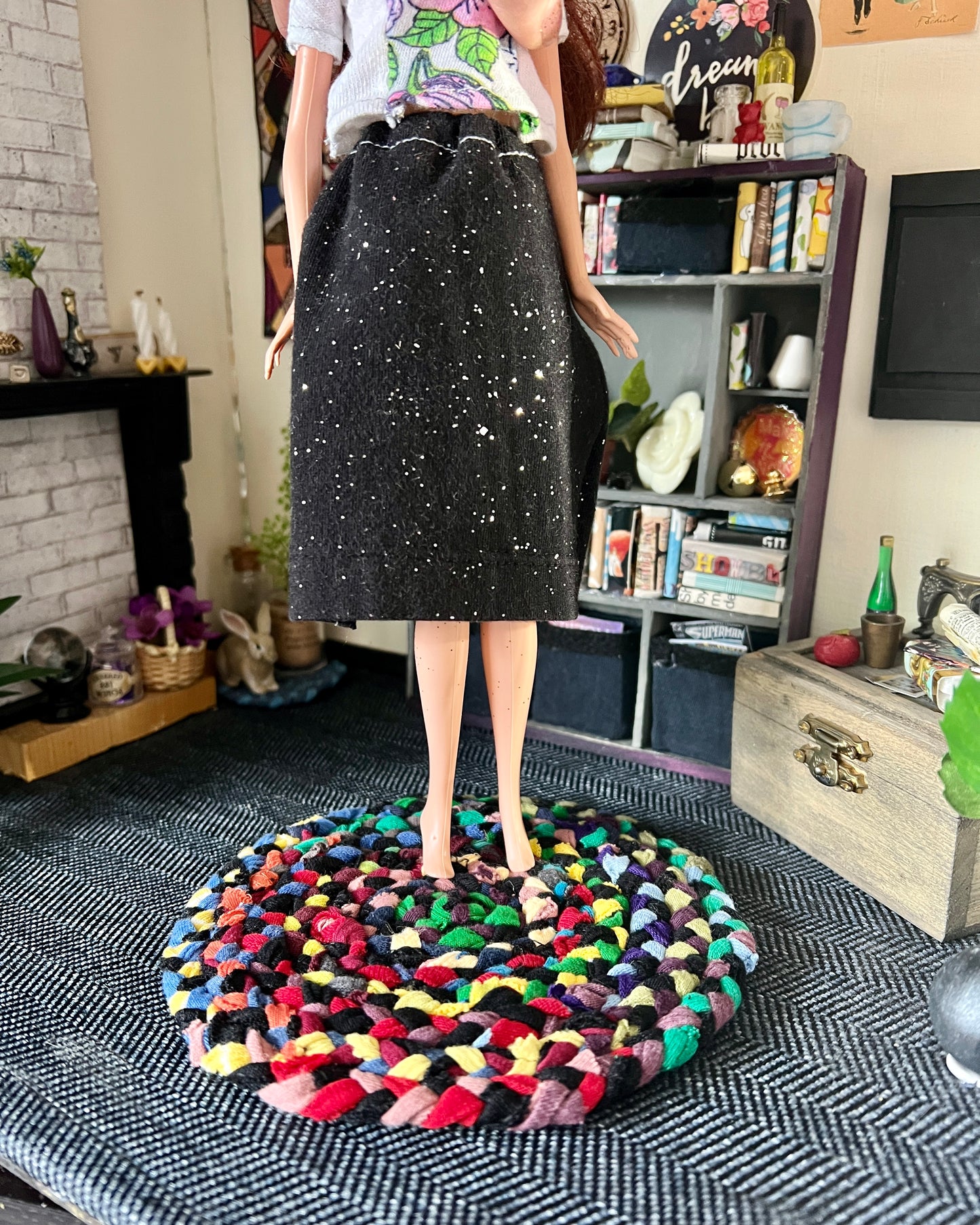 Barbie stands on top of a braided dollhouse rug, in a miniature room for scale and styling