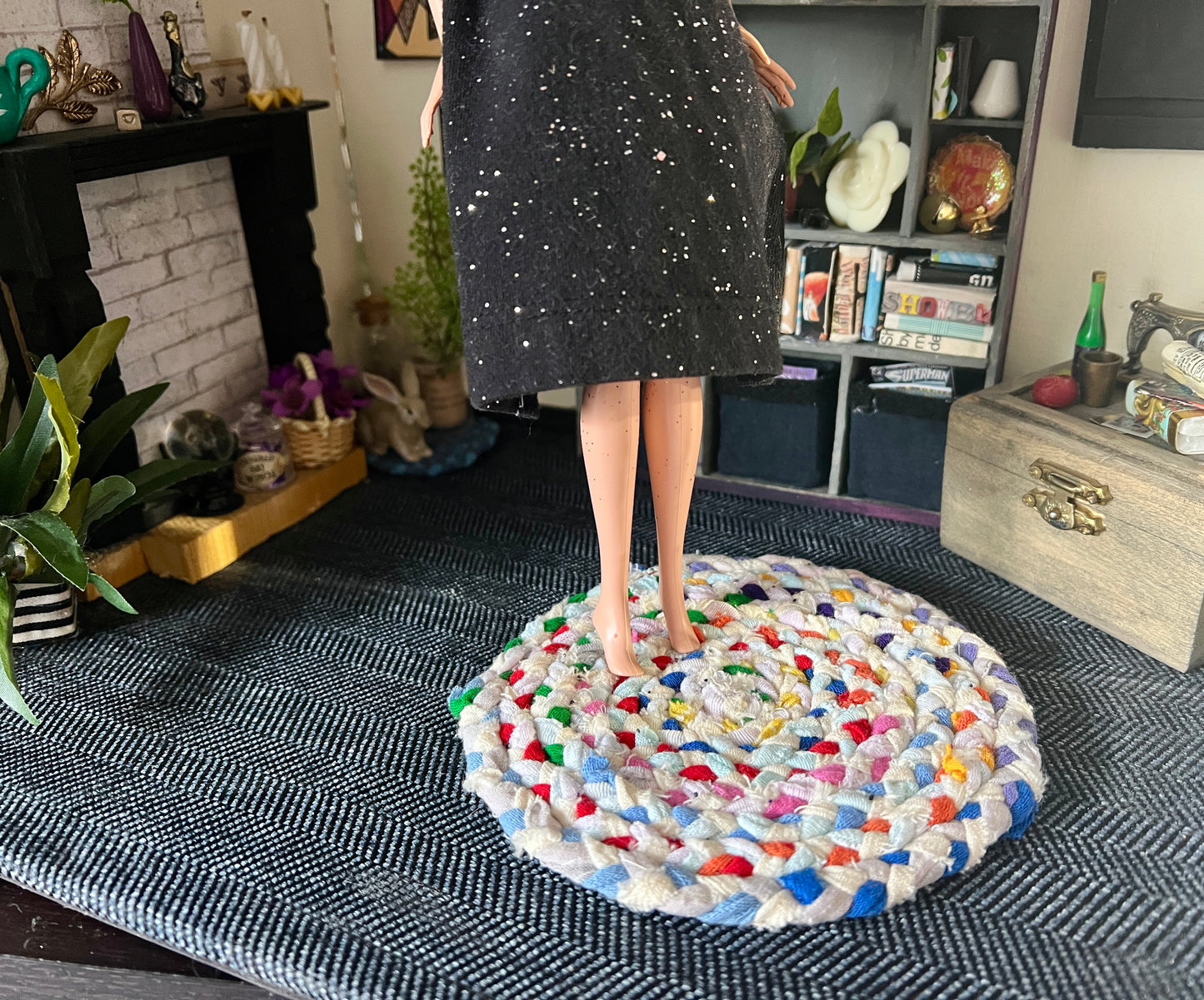 Barbie stands on top of a braided dollhouse rug, in a miniature room for scale and styling
