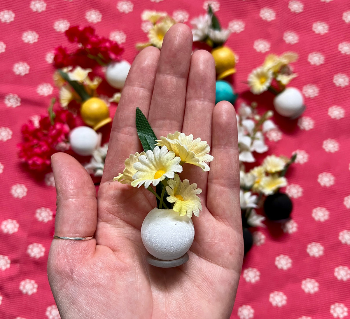 Hand holding a small decorative item with flowers against a polka dot background