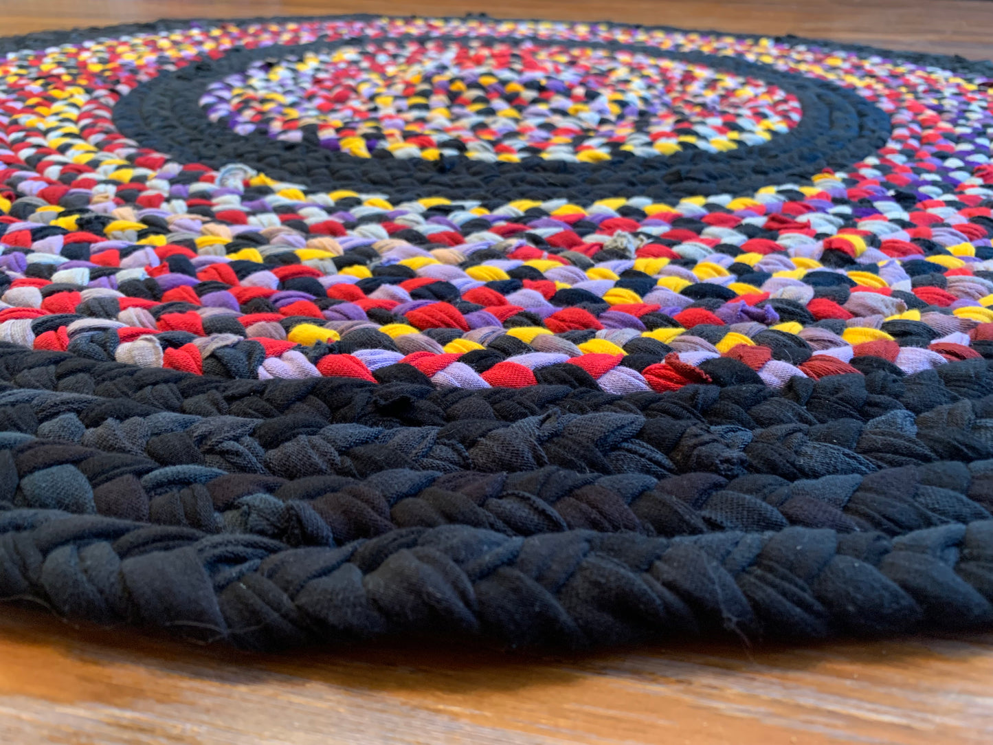 strands of tshirt in black, red, purple, golden yellow, and lavender have been hand braided and hand stitched together to form a rug