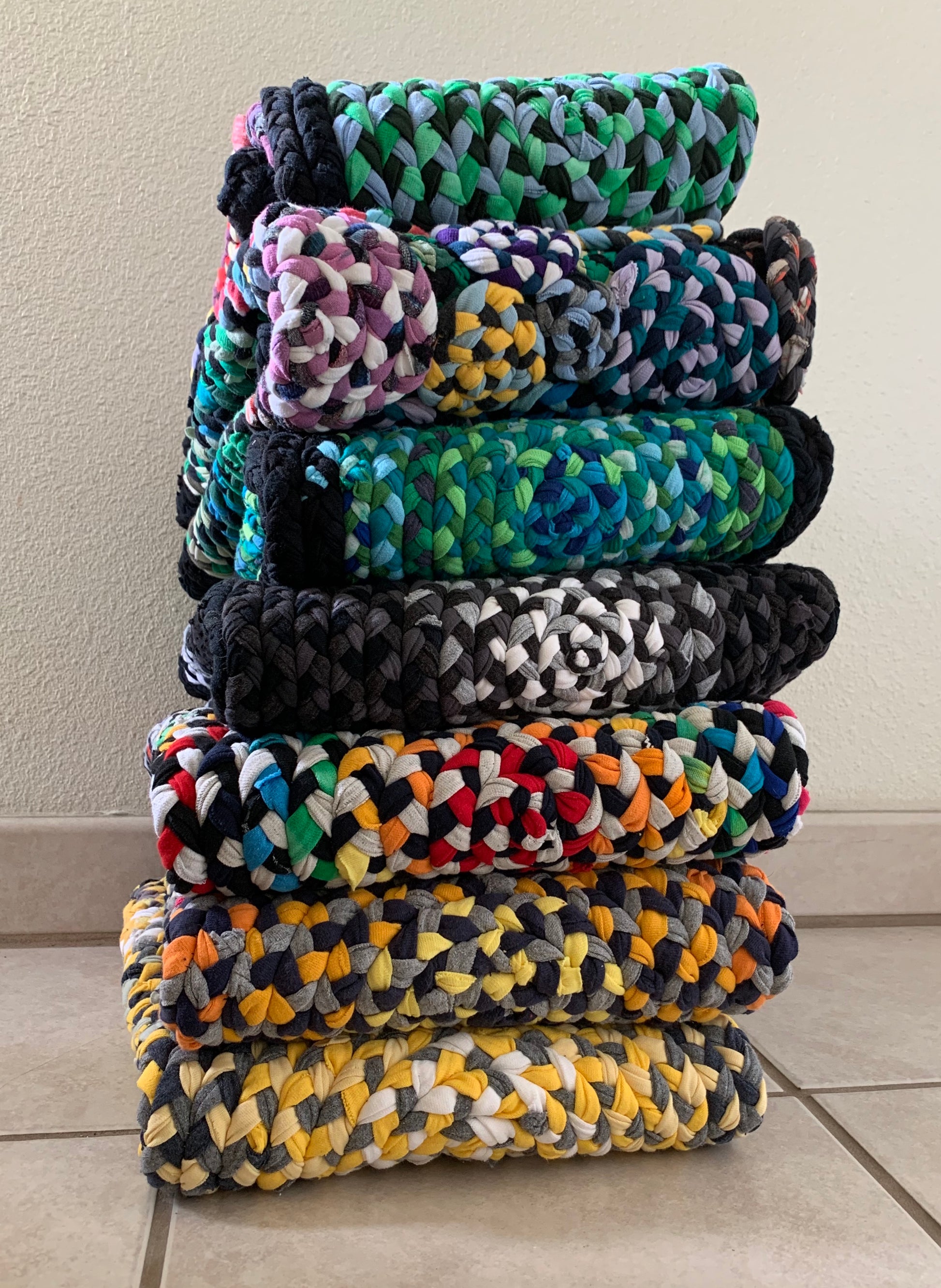 a stack of unique vibrant hand-braided and hand-sewn tshirt rugs on a tile floor