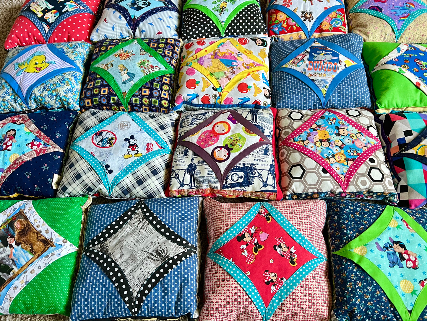 A collection of handmade patchwork baby pillows arranged in rows, featuring various colorful fabrics, various characters, polka dots, and floral prints.