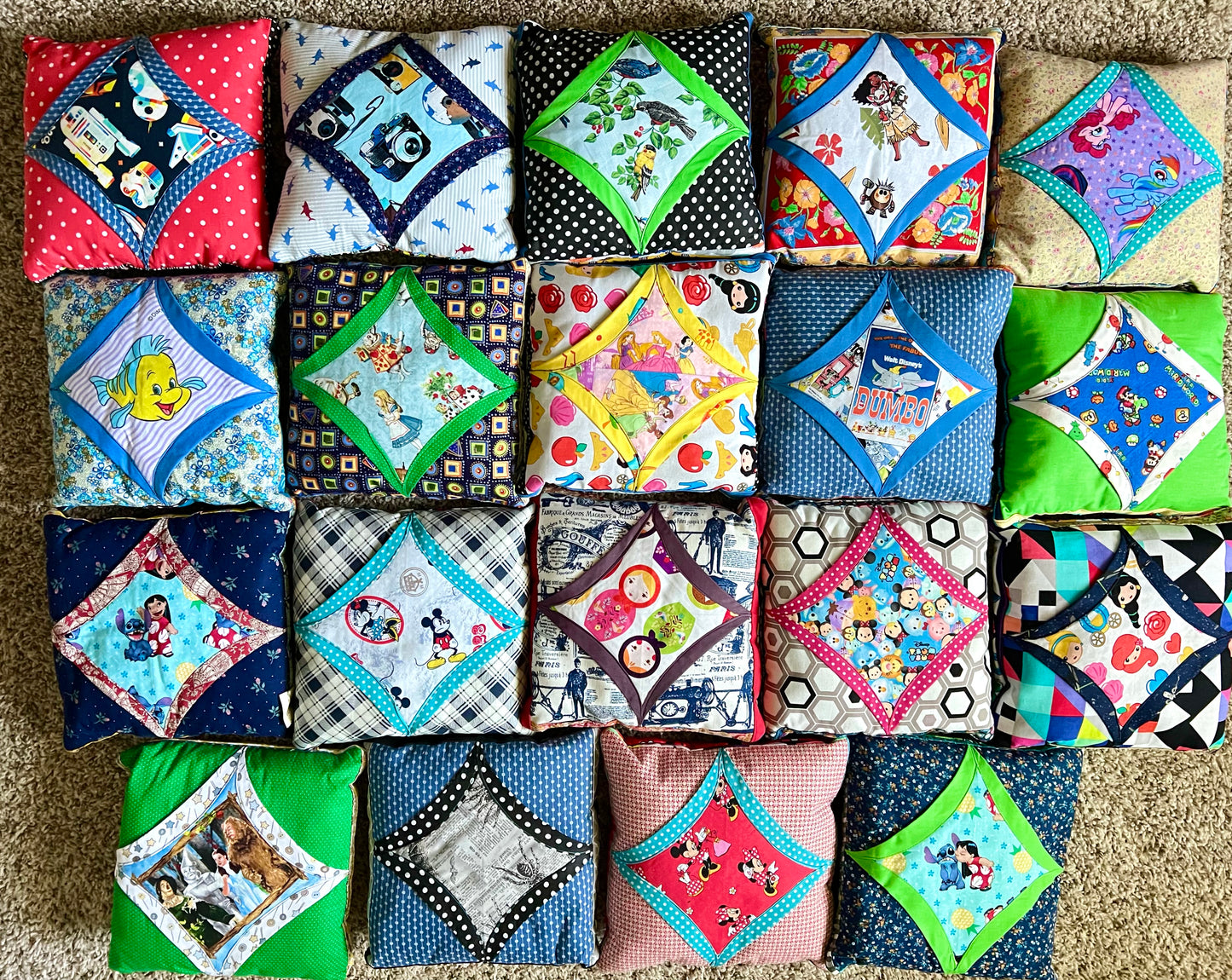 A collection of 20 handmade quilted fabric square pillows arranged in a grid on a beige carpet. Each pillow features a unique colorful pattern, including polka dots, floral prints, cartoon characters, and family photos, making the overall color identity highly multicolored.