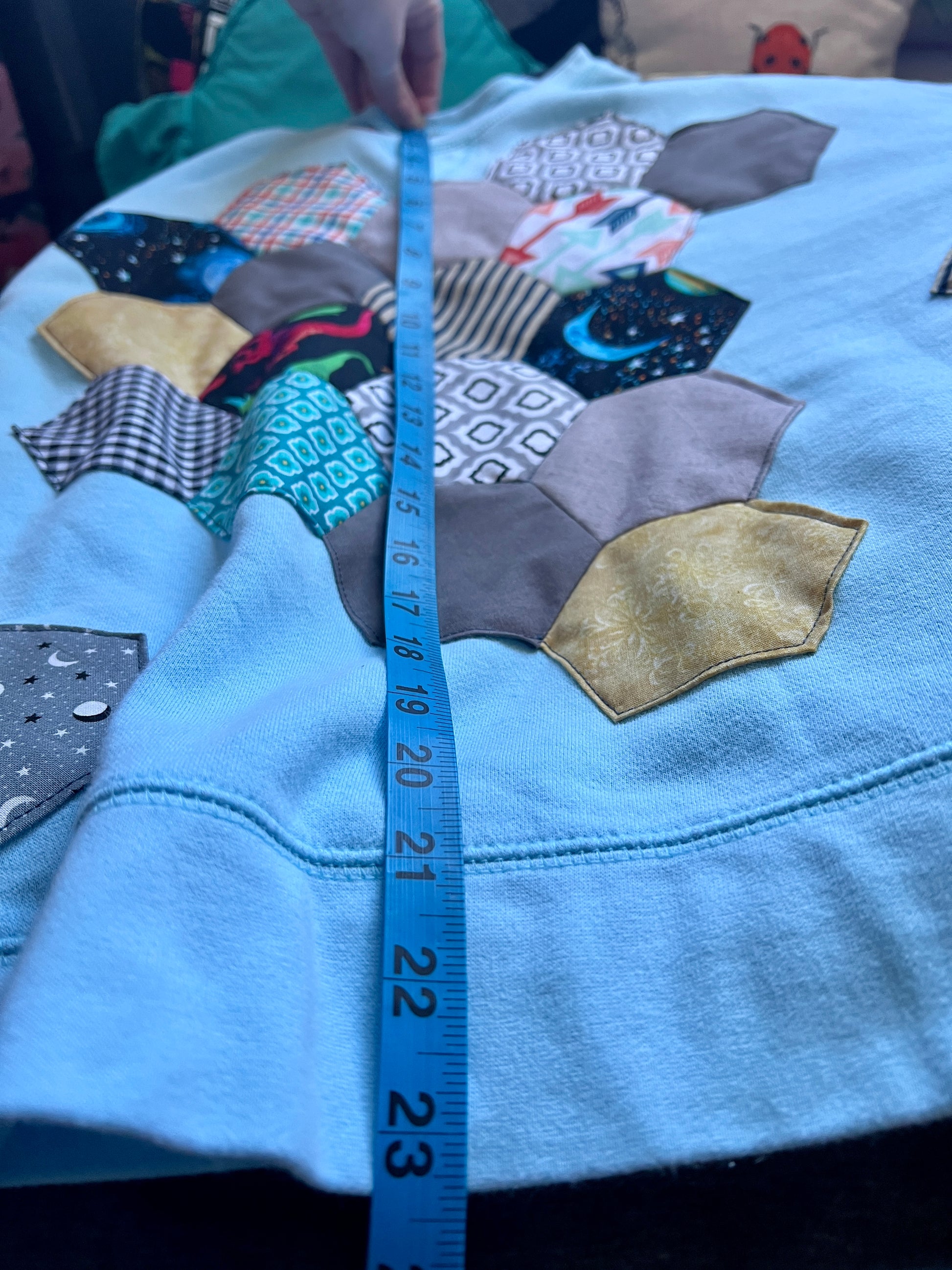 Patchwork fabric with various patterns and a measuring tape on a blue crewneck