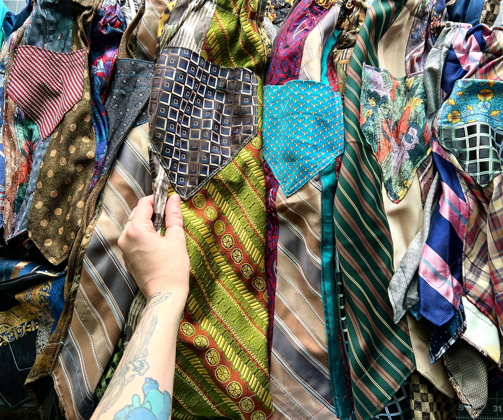 Hand holding a necktie skirt amidst a collection of colorful necktie skirts with pockets