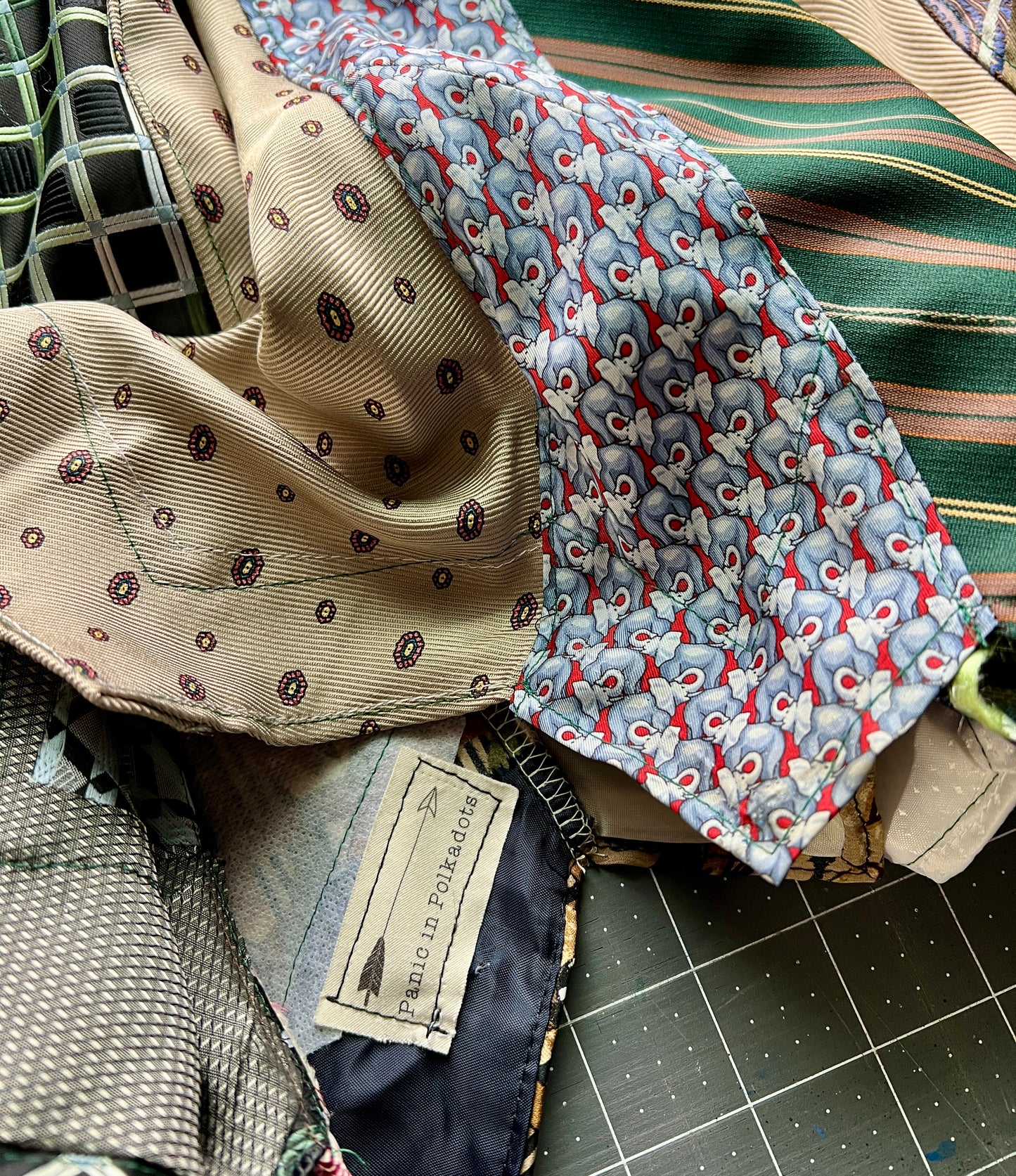 Collection of patterned neckties which have been made into a skirt, on a cutting mat with a visible brand tag.