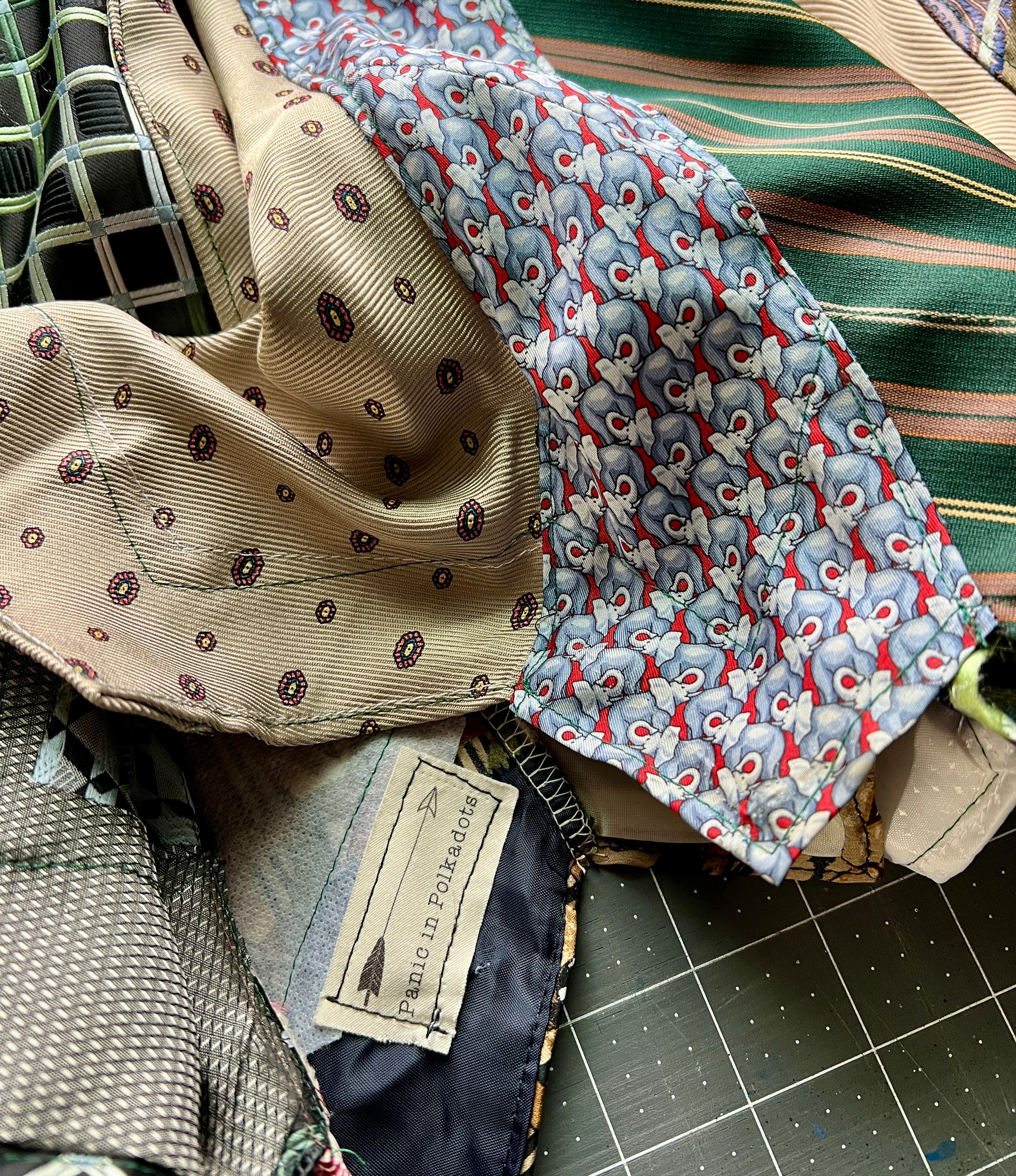 Collection of patterned neckties which have been made into a skirt, on a cutting mat with a visible brand tag.
