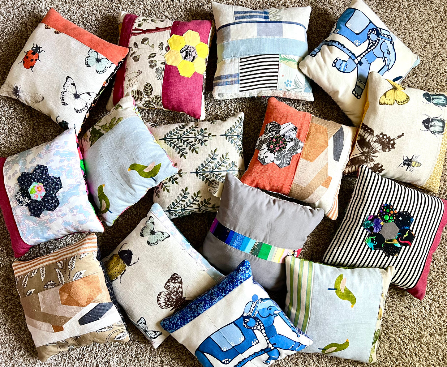 A collection of handmade patchwork throw pillows in various colors and patterns, arranged on a beige carpet.
