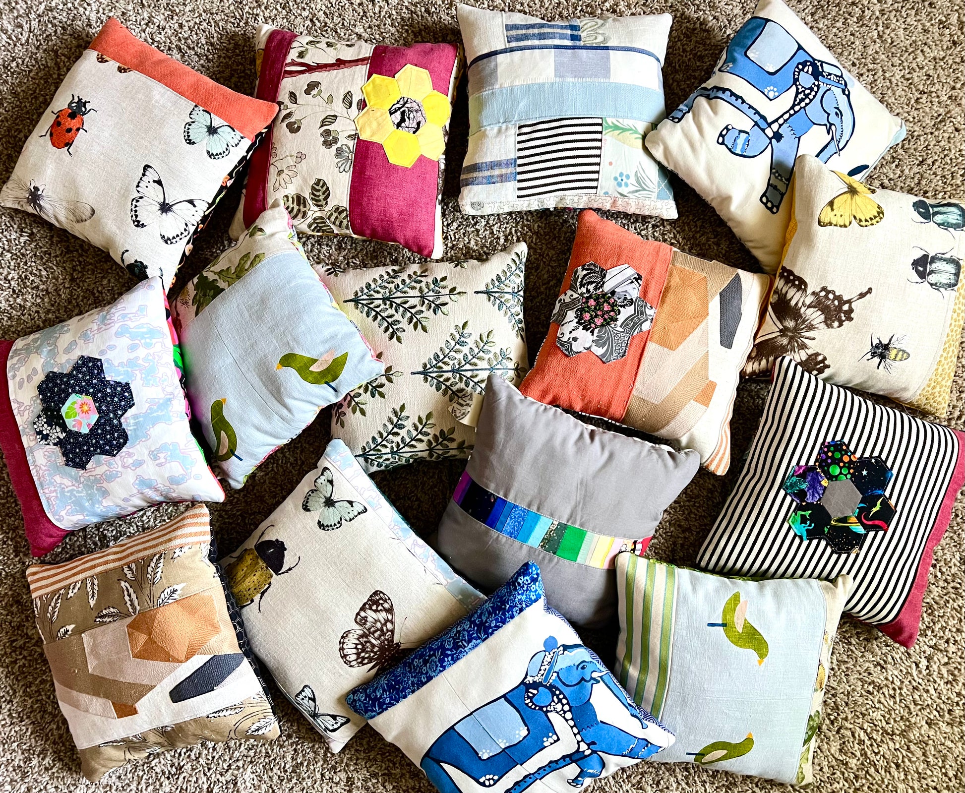A collection of handmade patchwork throw pillows in various colors and patterns, arranged on a beige carpet.