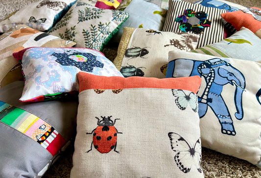 A collection of handmade, multi-colored fabric throw pillows with various animal and nature prints, including a prominent central beige pillow with a red ladybug and butterfly pattern.
