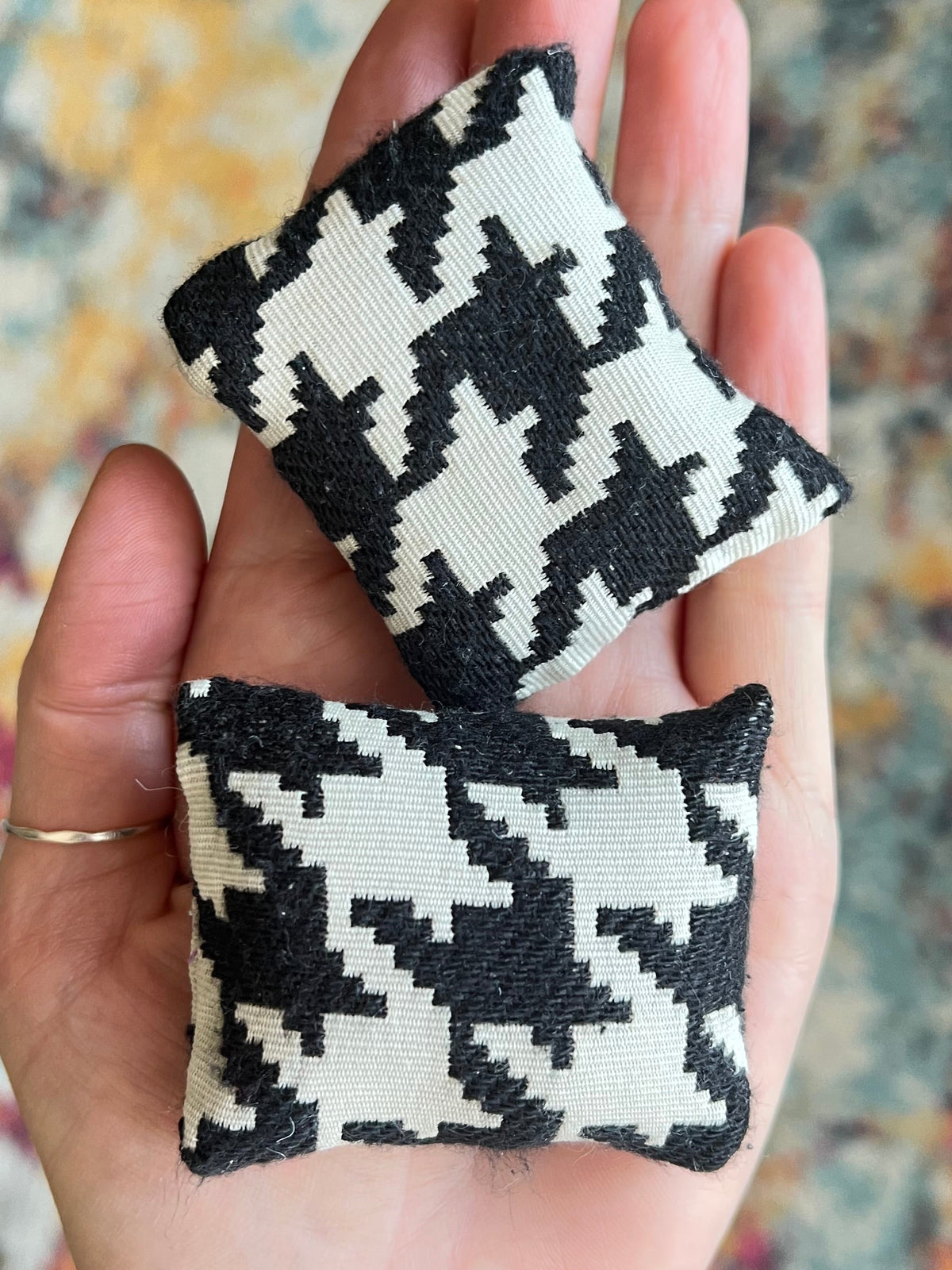 Two black and white patterned fabric squares held in a hand with a blurred background.