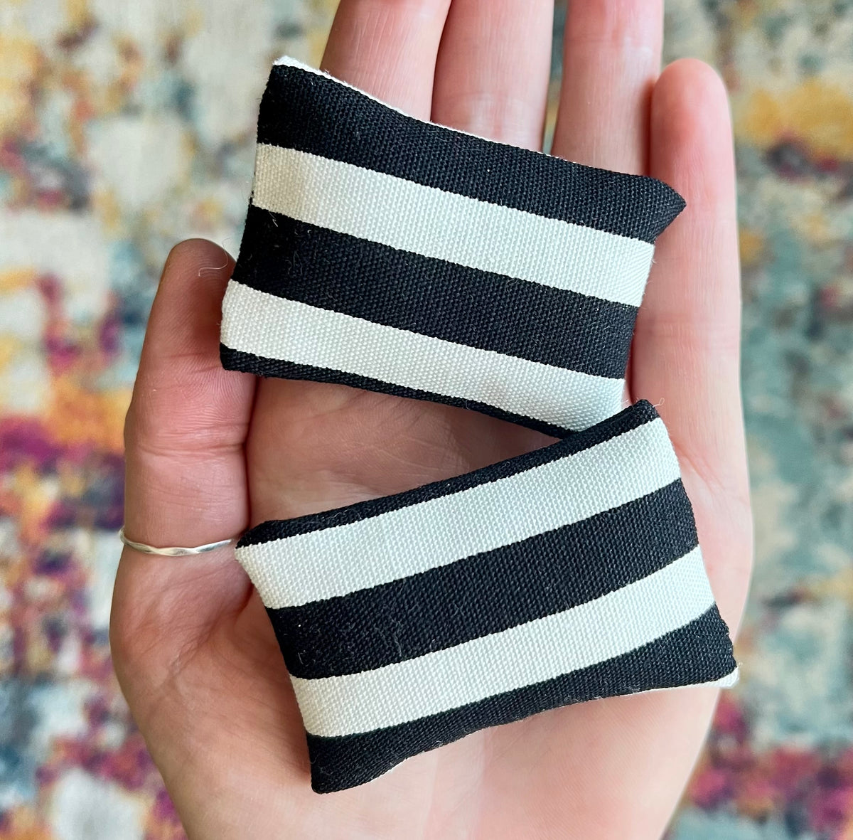 Black and white striped fabric doll pillows held in a hand with a colorful background