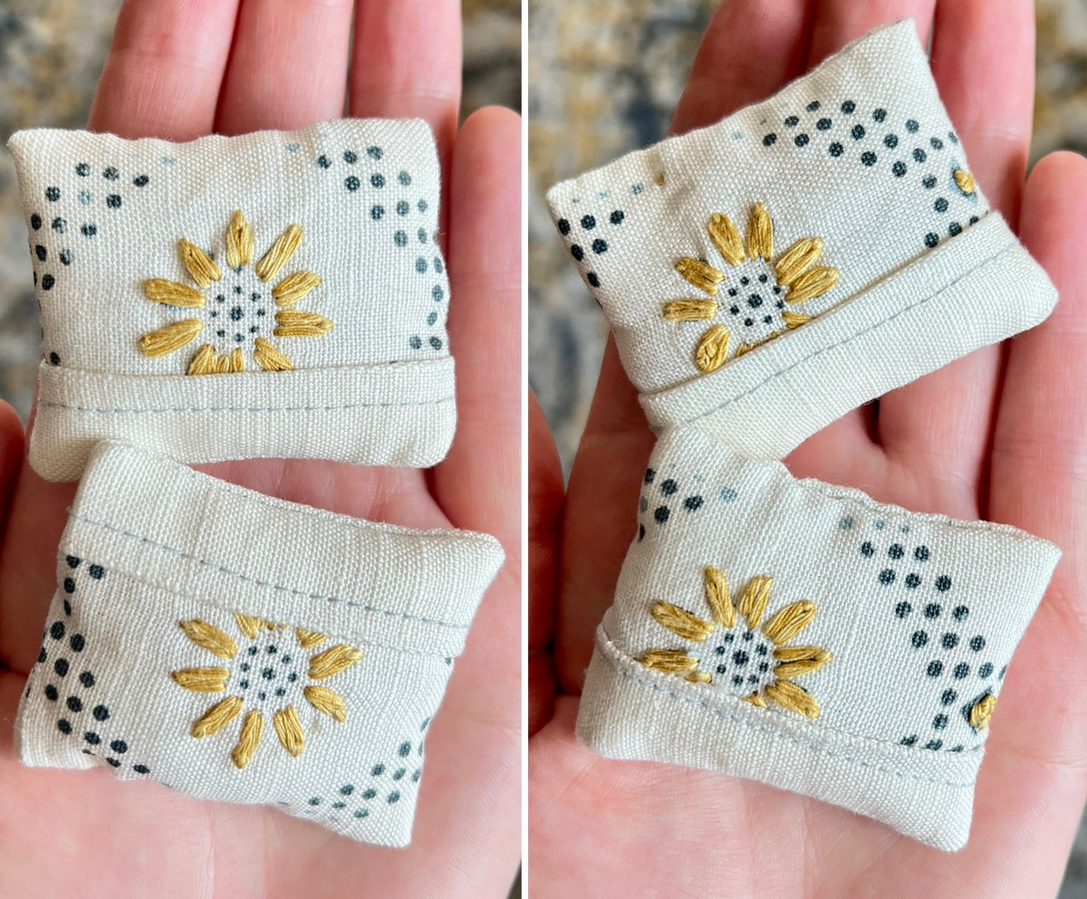 Two small fabric doll pillows with sunflower embroidery held in hands.