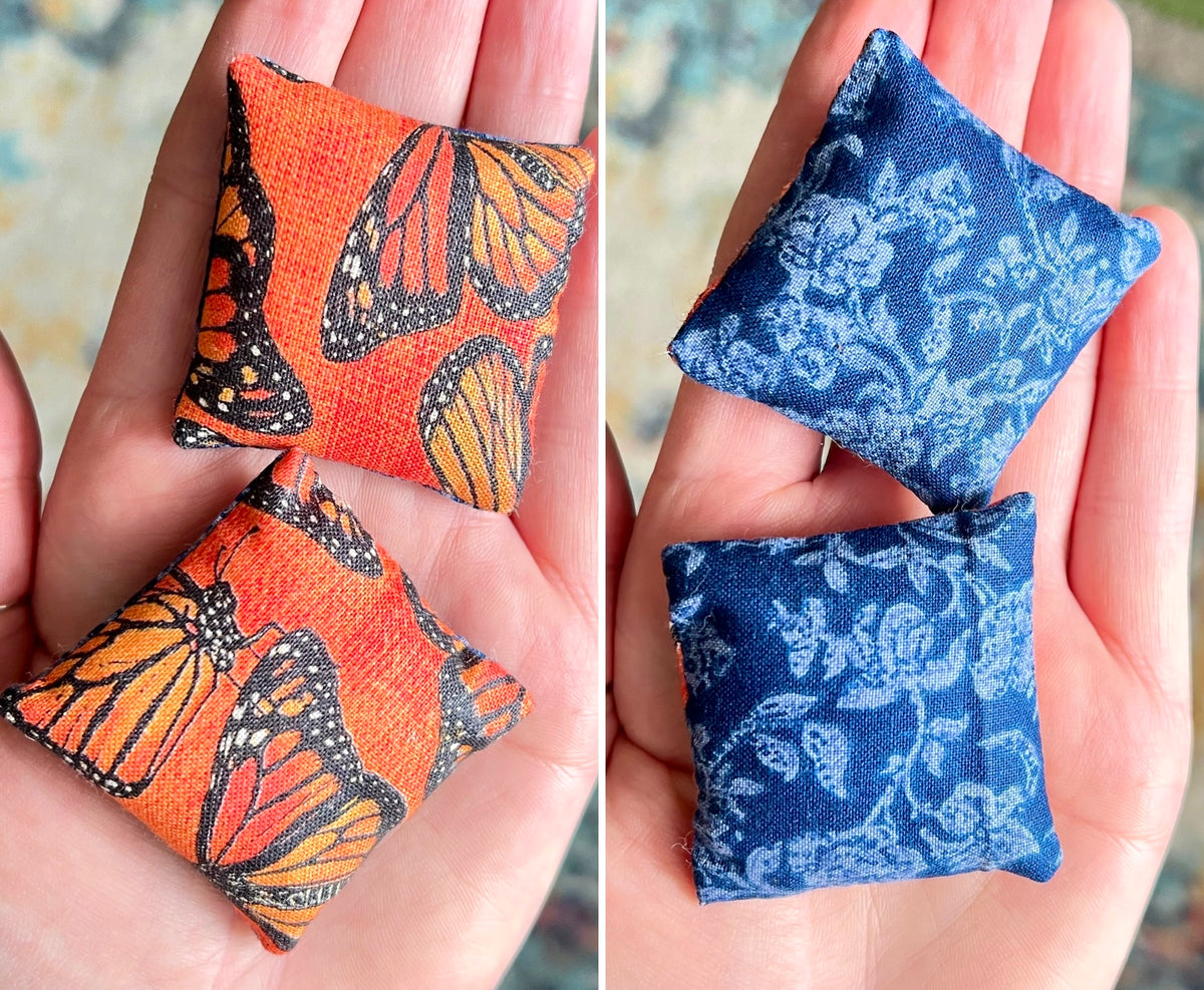 Two small fabric doll pillows, front with butterfly pattern and the back with floral pattern, held in hands.