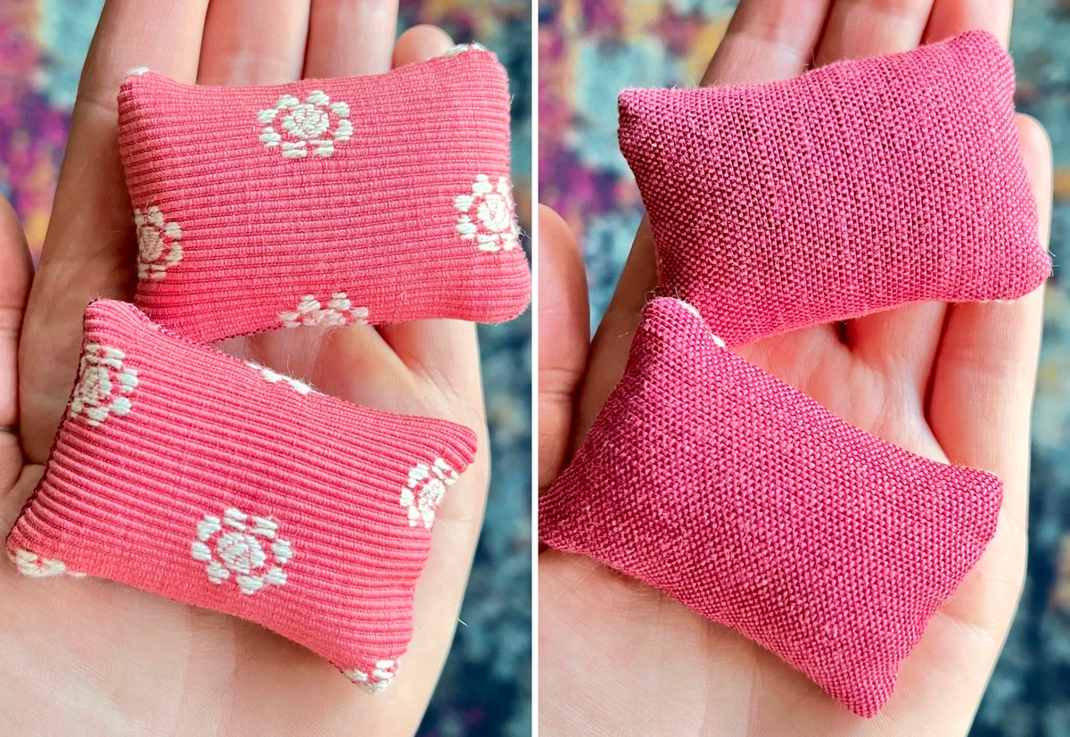 Two pink fabric doll pillows with white floral patterns held in hands against a blurred background.