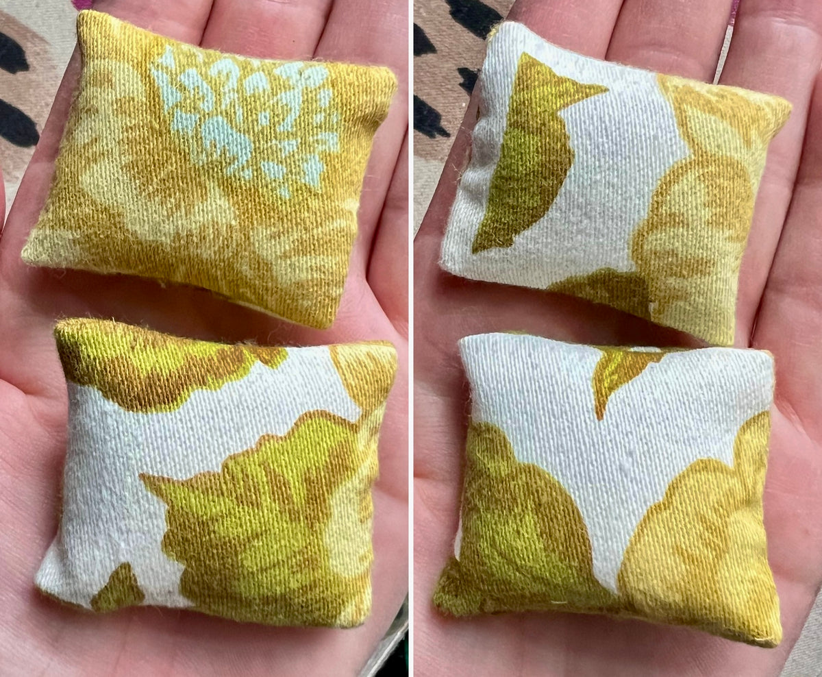 Two small fabric pillows with yellow leaf pattern held in hands.