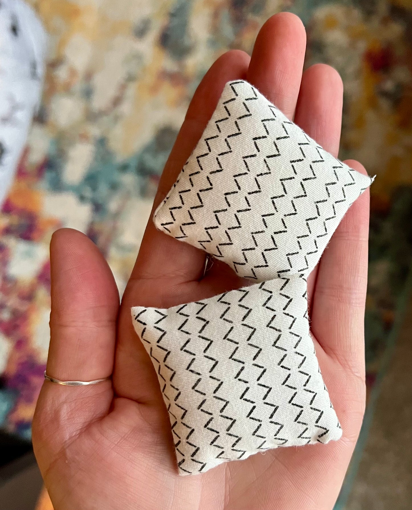 Small fabric pillows in various colors held in a hand for scale, white with black chevron pattern