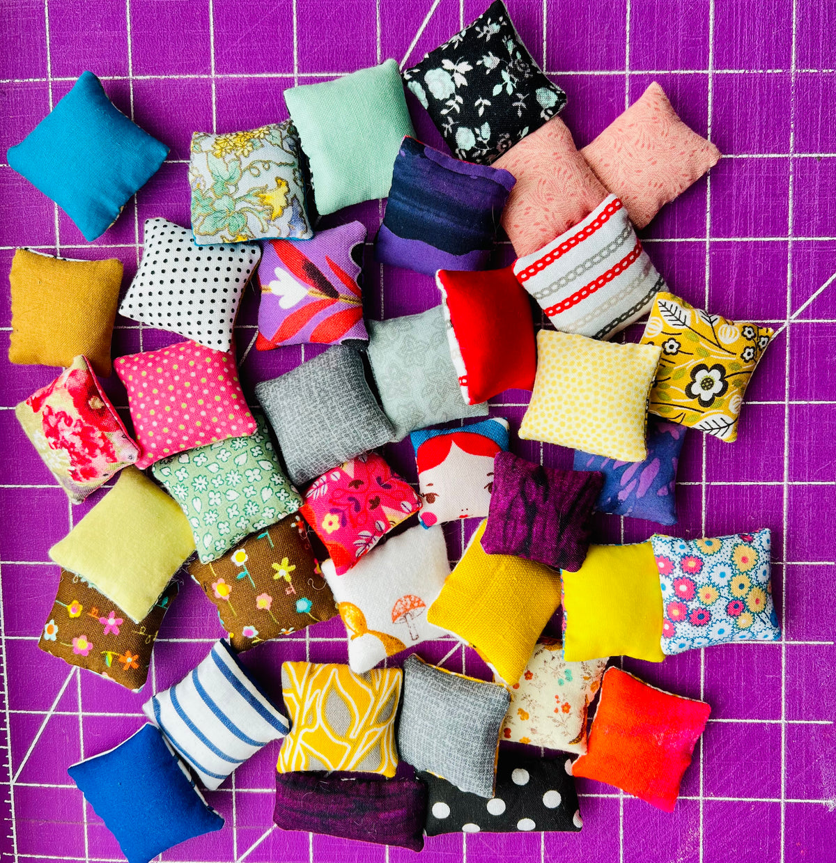 Assorted colorful fabric pillows on a purple grid background